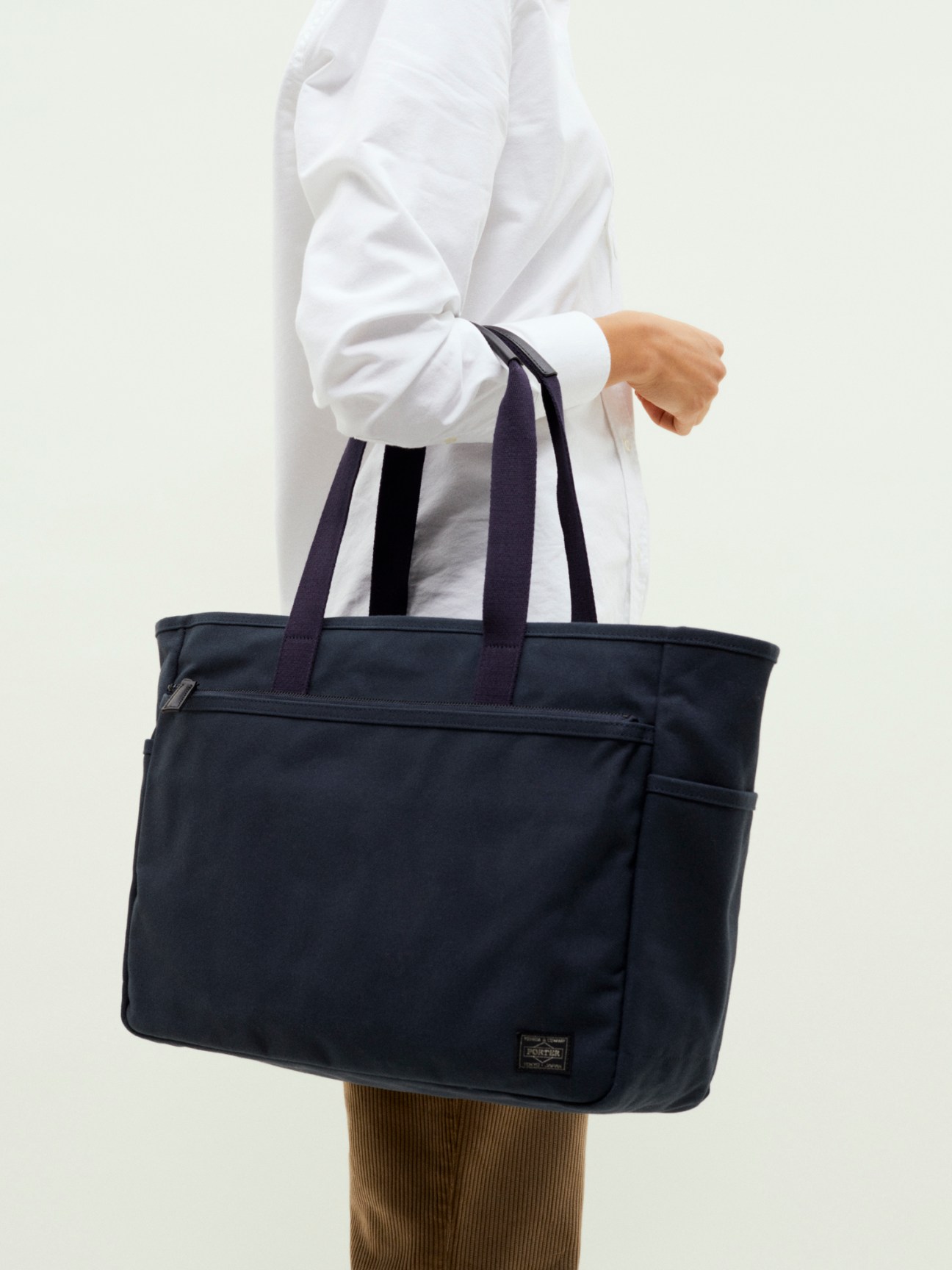 Person wearing white shirt carrying navy Porter x Monocle travel tote bag with shoulder straps.