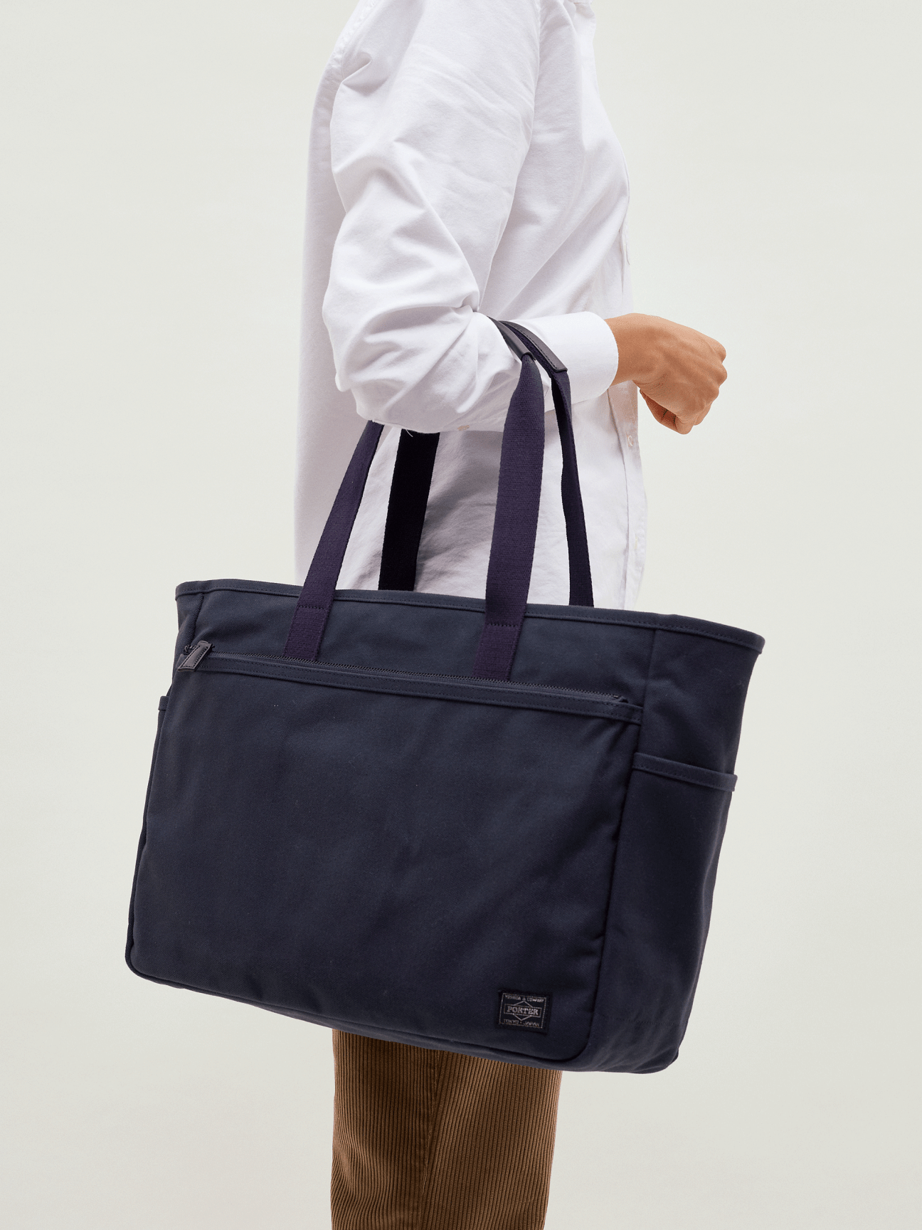Person in white shirt holding navy canvas Porter x Monocle travel tote bag with shoulder straps