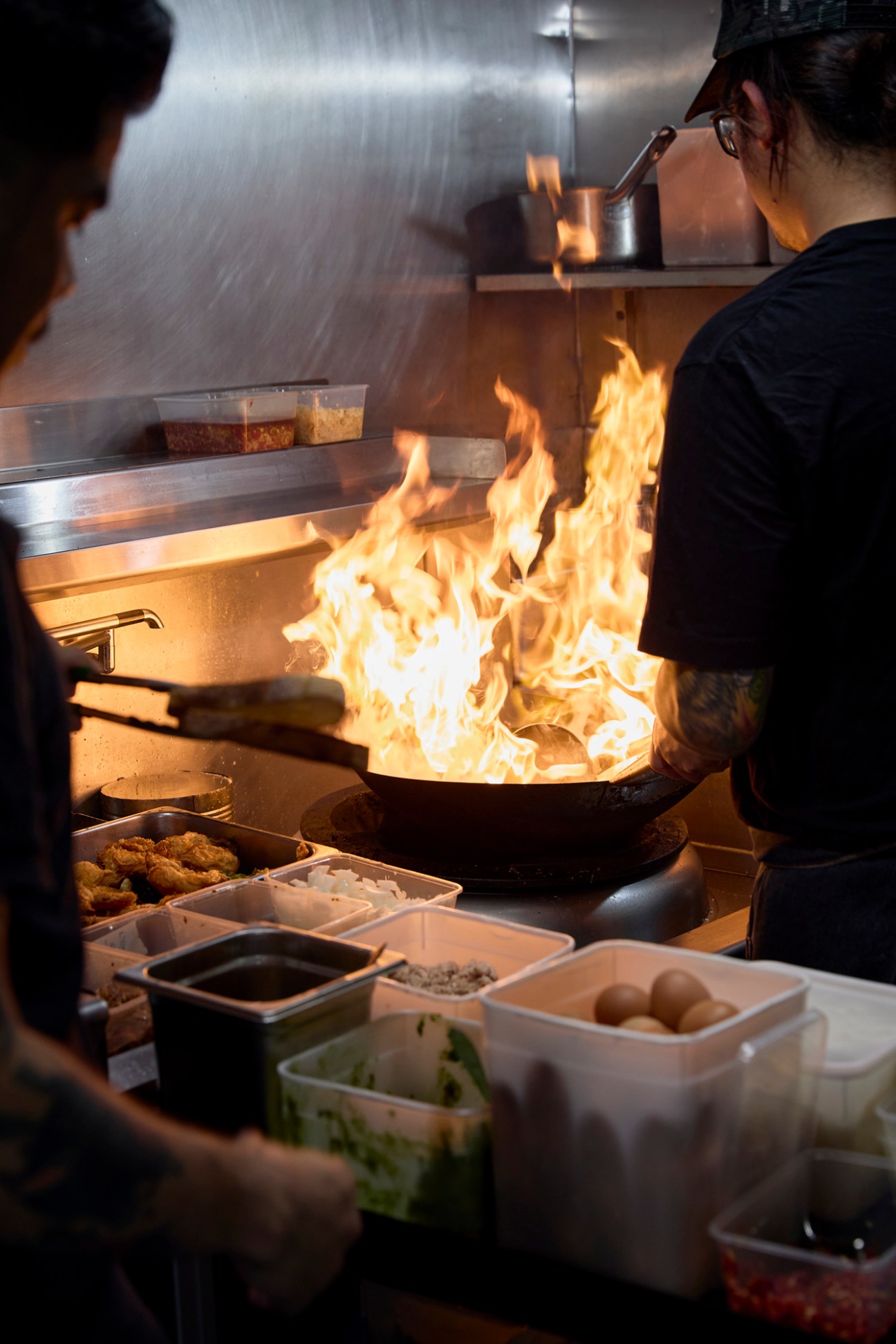Chef cooking with flames in a wok at West End Coffee House kitchen with ingredients visible