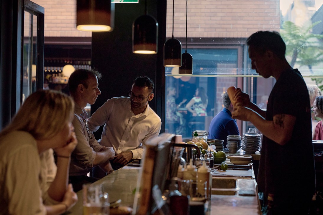 People enjoying drinks at a modern bar counter with pendant lighting and large windows