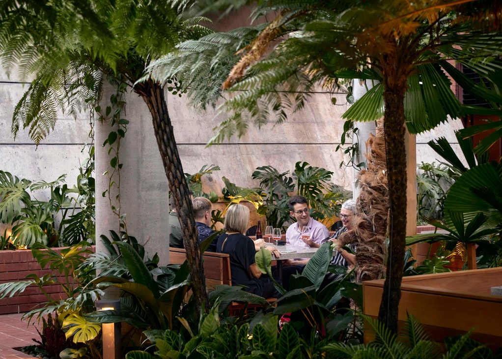 People dining at outdoor tables surrounded by lush tropical plants and palm trees