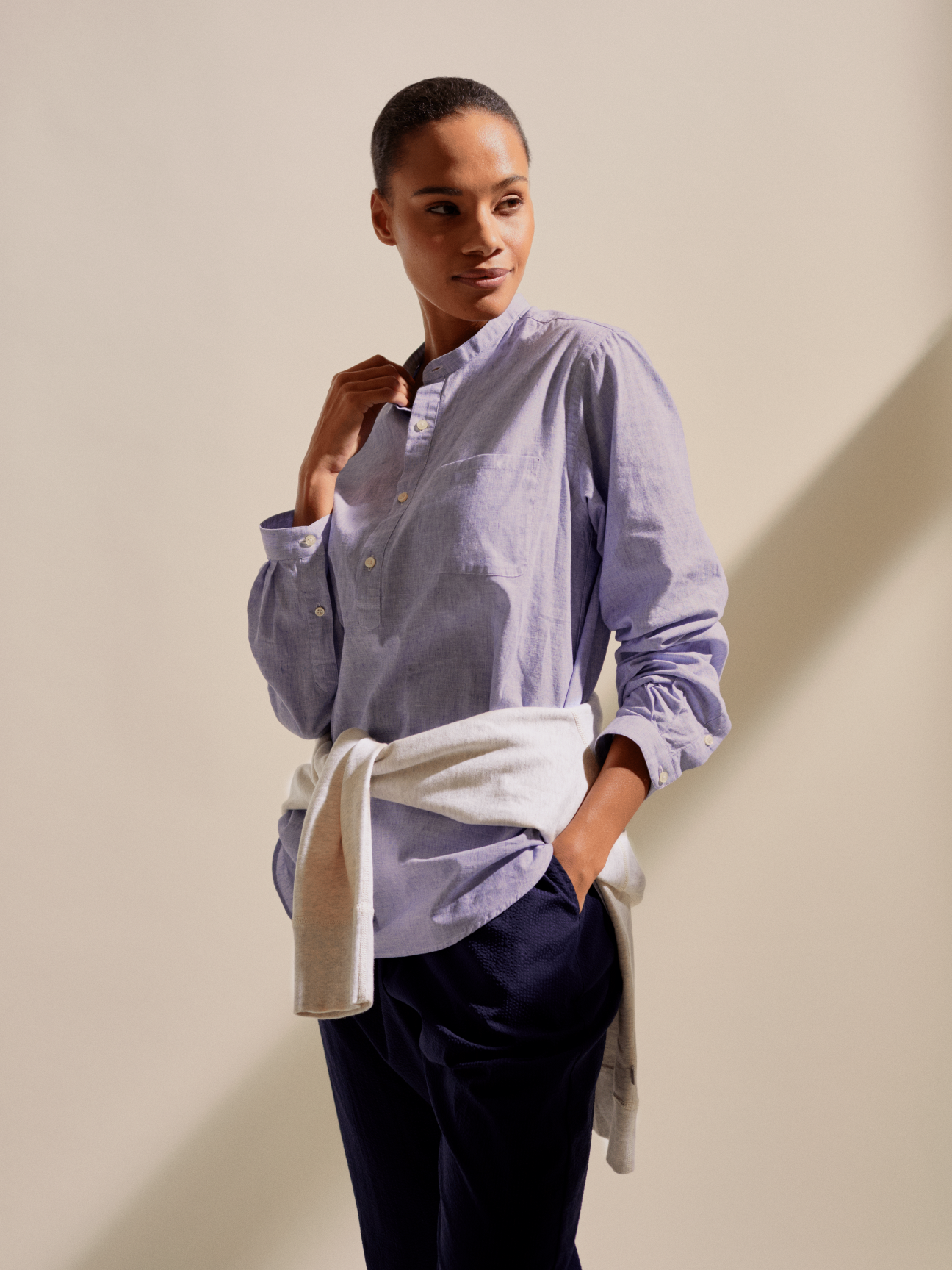 Woman wearing pale blue grandad-collar shirt with navy trousers and cream cardigan tied around waist