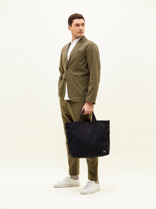 Man wearing olive seersucker blazer and trousers by Smock x Monocle, holding a black tote bag.