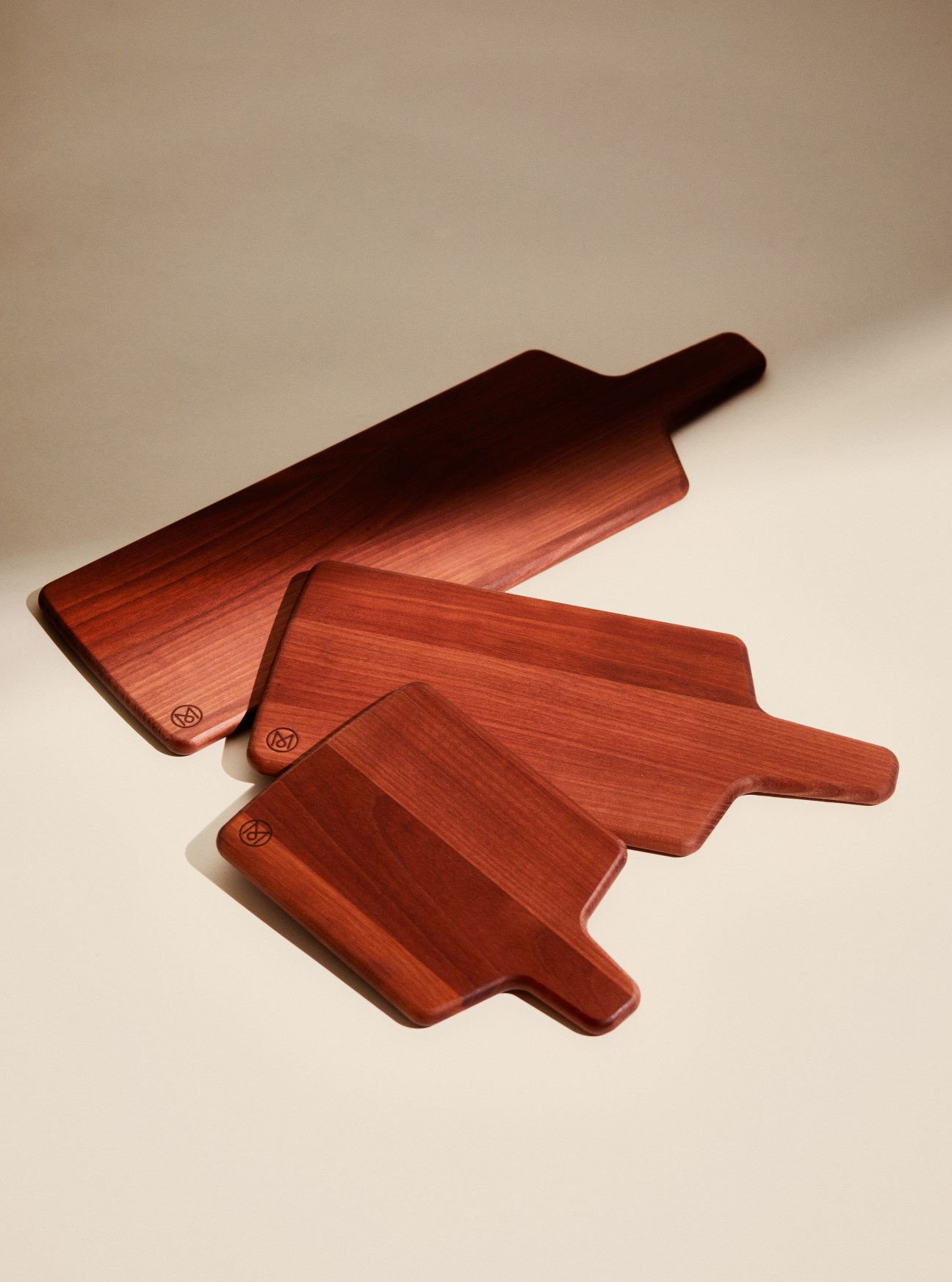 Set of three Swiss cherry wood apéro boards in varying sizes with handles arranged on neutral background