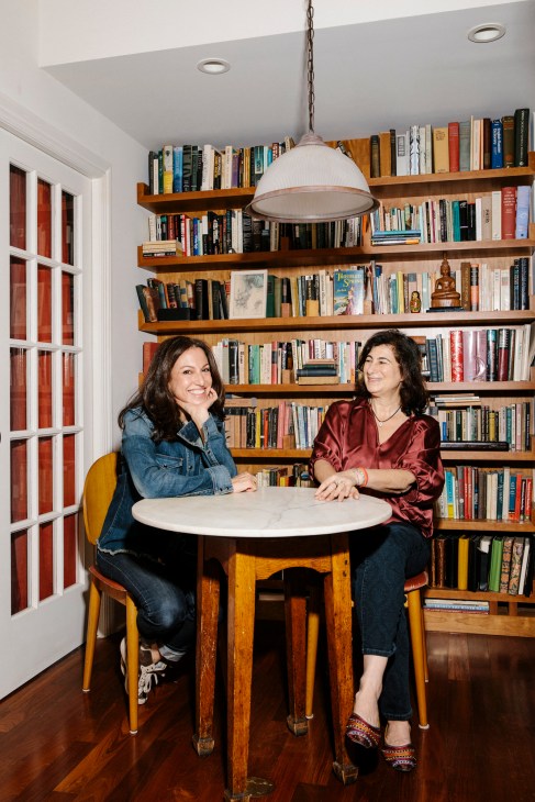 Cindy Spiegel and Julie Grau sit at a round table in front of wooden bookshelves in their office.