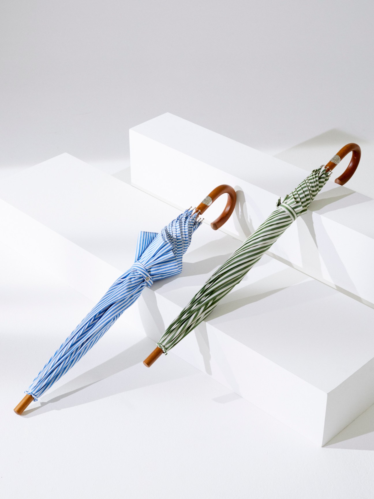 Two elegant umbrellas with striped patterns and wooden handles positioned on white geometric blocks