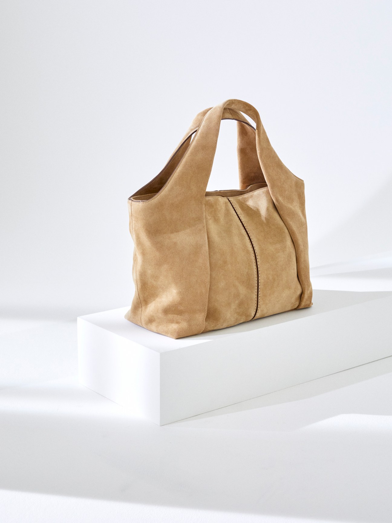 Tan suede handbag by Tod's displayed on white surface