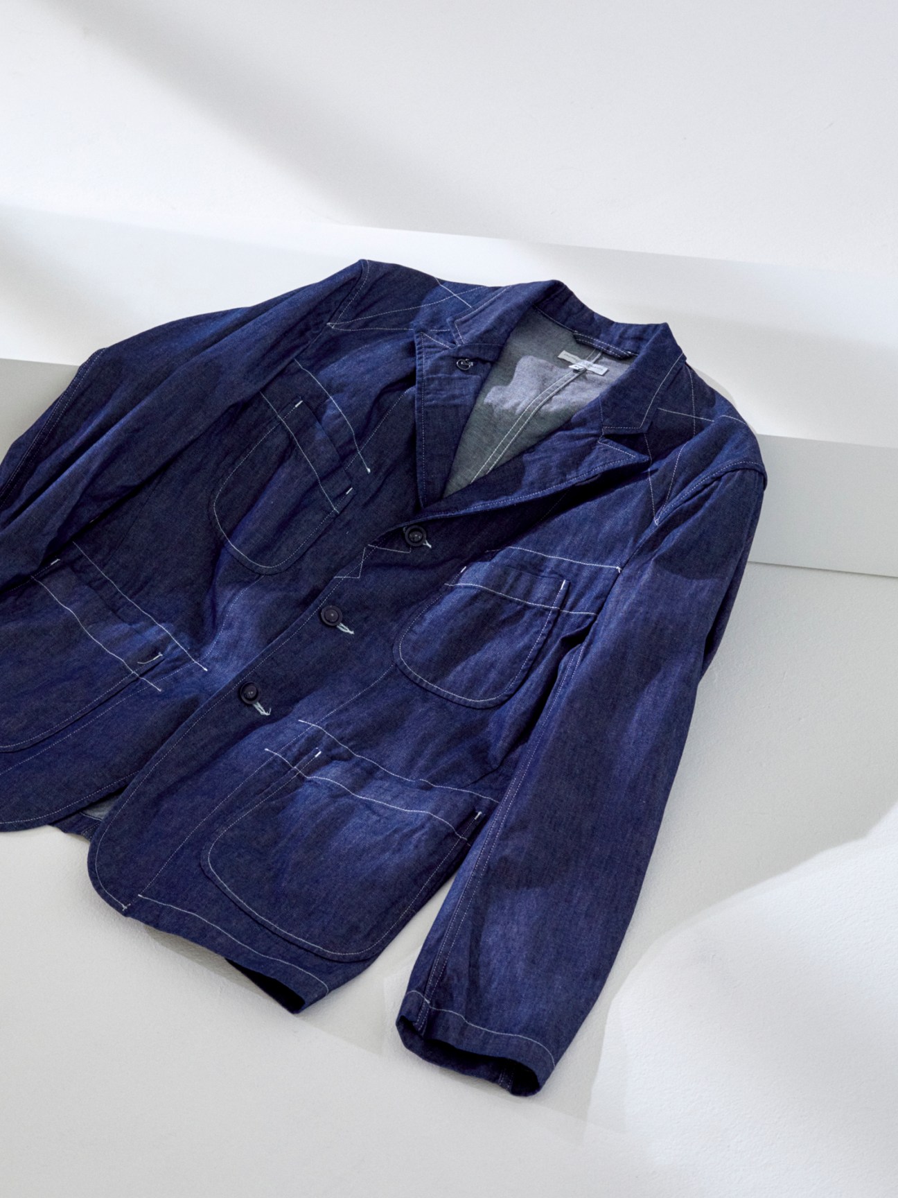 Dark blue denim jacket with multiple pockets and contrast stitching laid flat on white surface