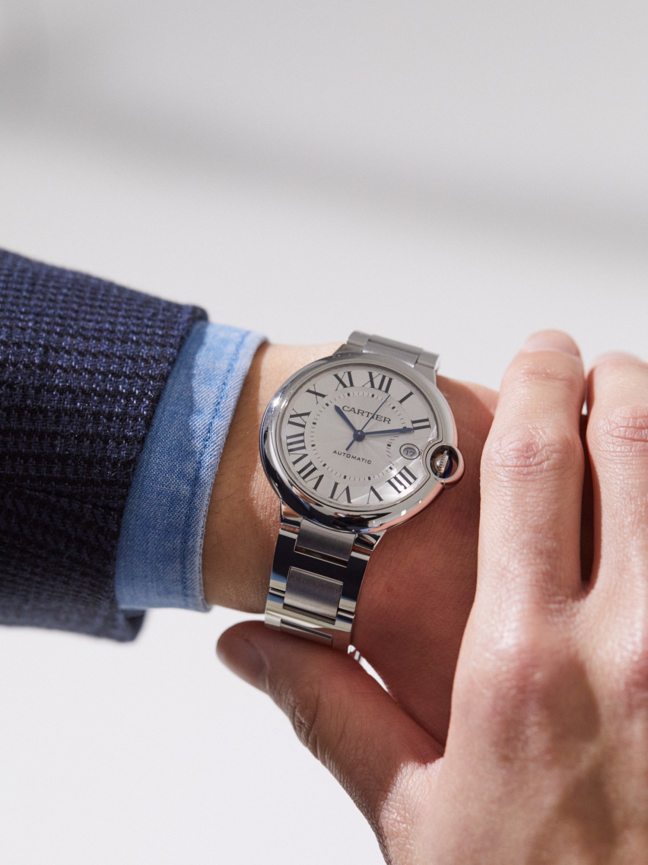 Person wearing Cartier Ballon Bleu watch with Roman numerals on wrist alongside Brooksfield jacket and shirt