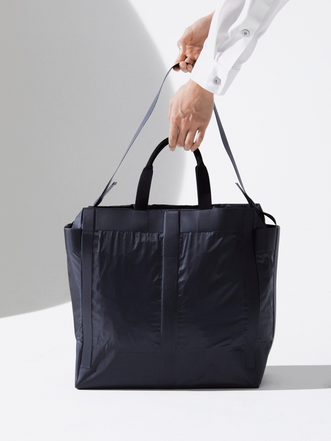 Person in white shirt holding dark navy tote bag with shoulder strap