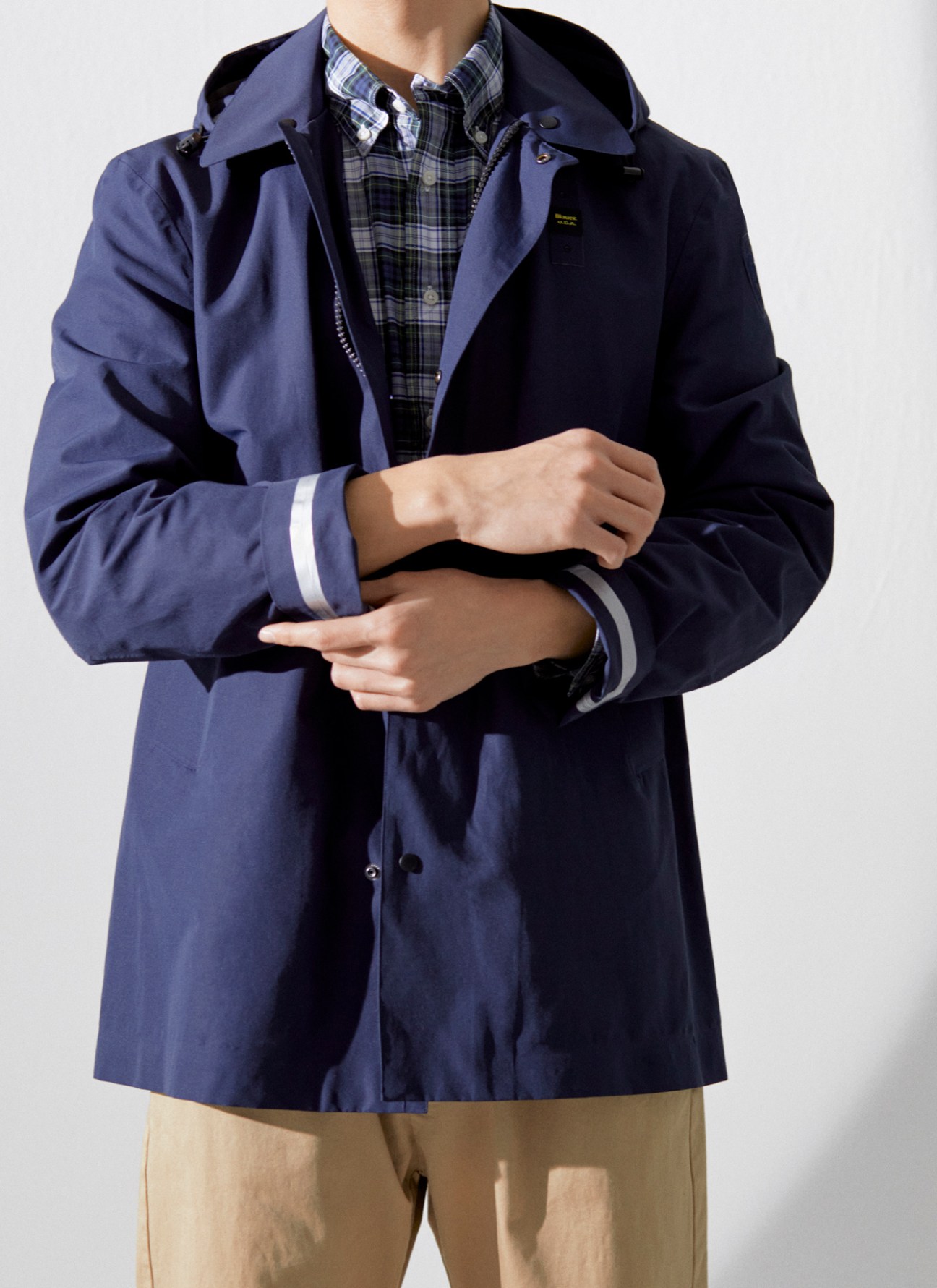Navy blue hooded jacket with zip closure worn over plaid shirt and khaki trousers