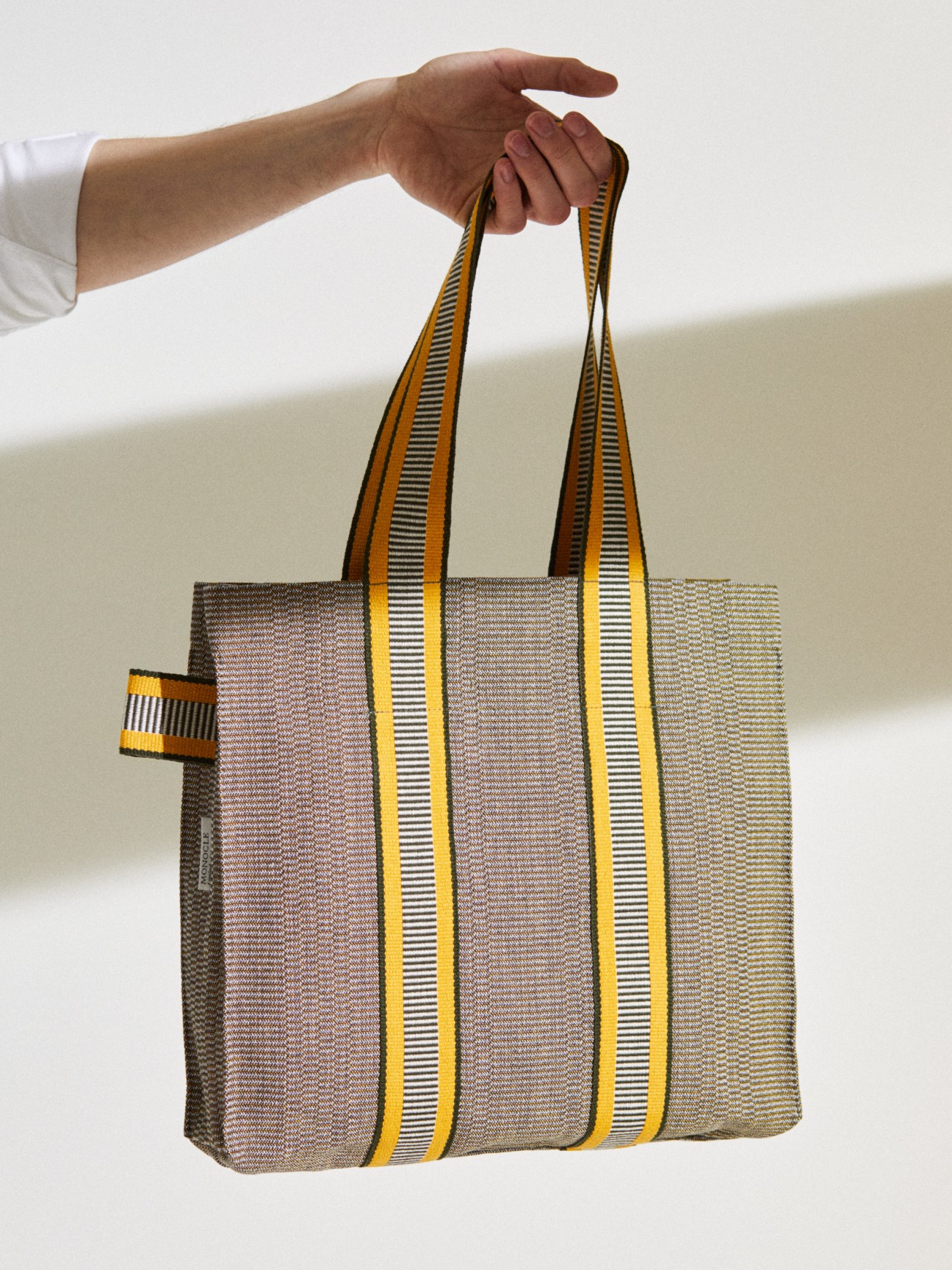 Hand holding grey and yellow striped tote bag with geometric pattern and matching handles