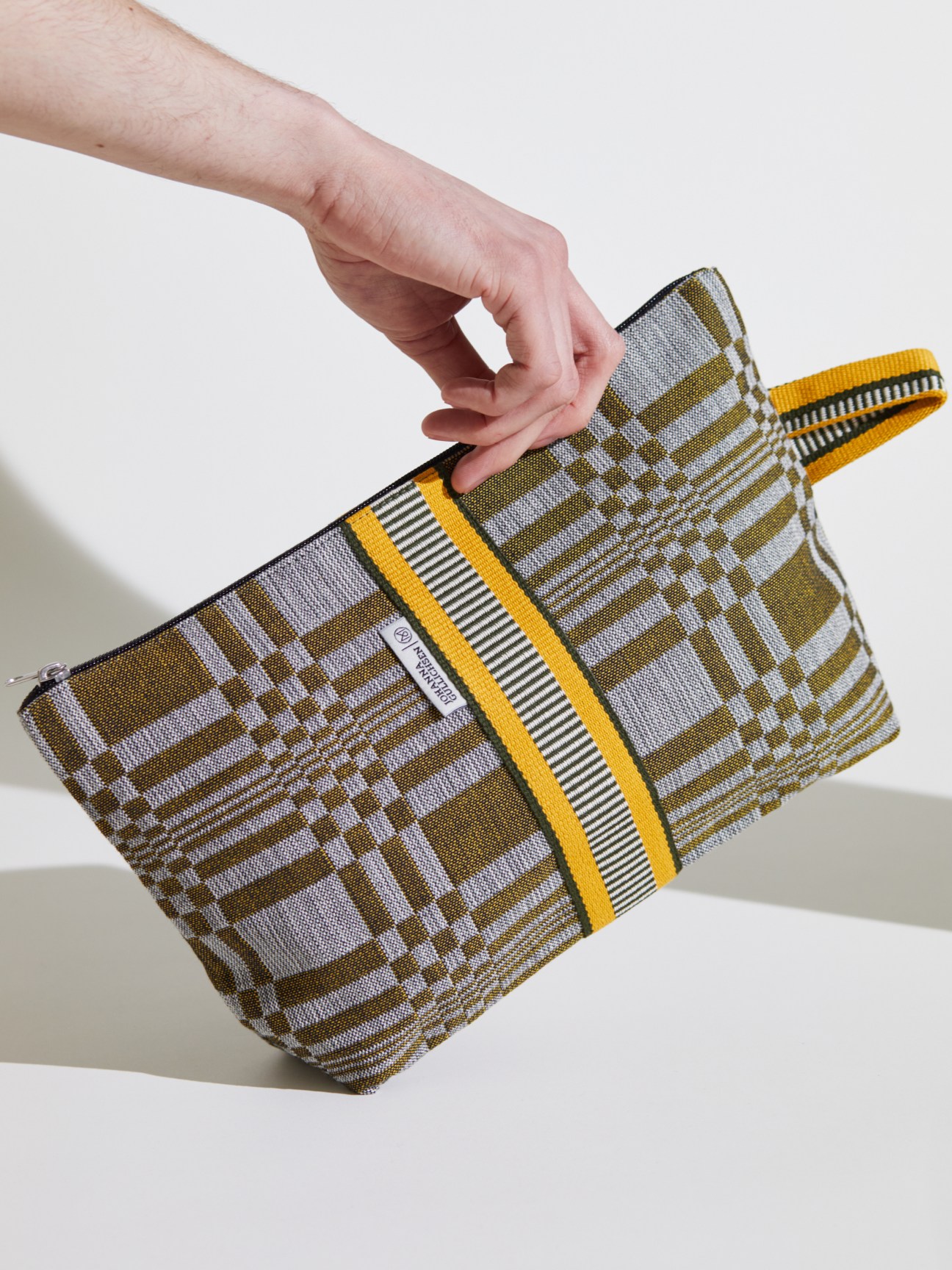 Hand holding striped textile vanity case with yellow and grey pattern and zipper closure