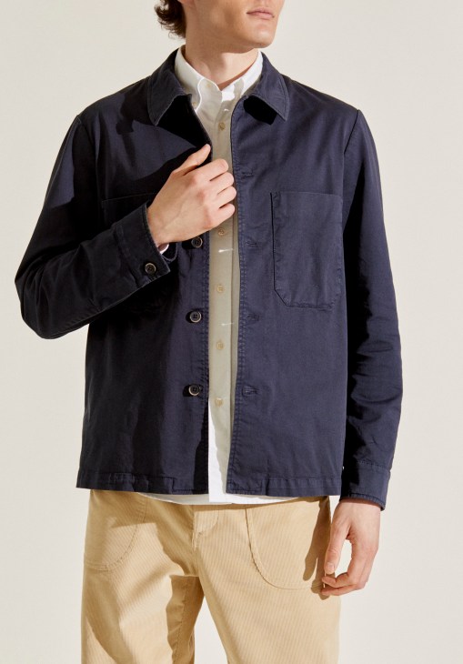 Man wearing navy cotton overshirt by Barena x Monocle over cream shirt and tan trousers.