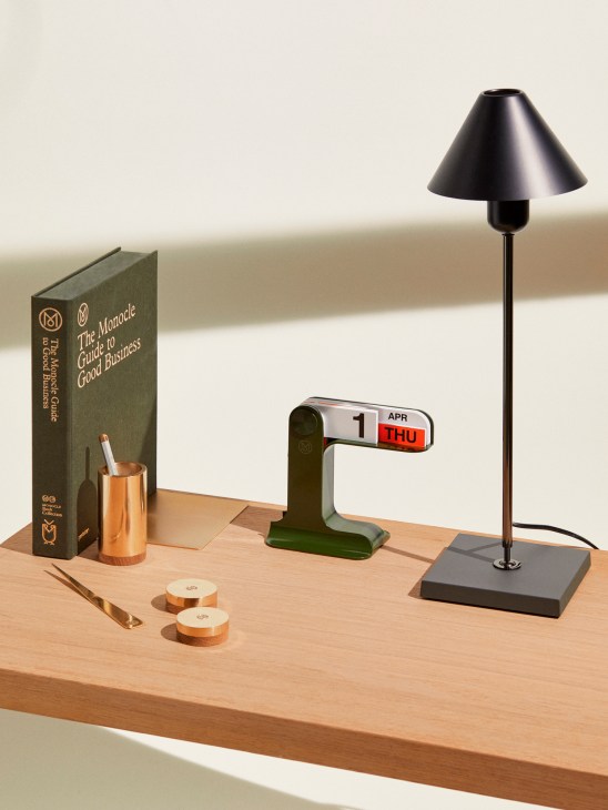 Desk setup with Monocle Guide to Good Business book, perpetual calendar, brass pen pot, paperweights, letter opener, and Gira desk lamp by Santa & Cole.