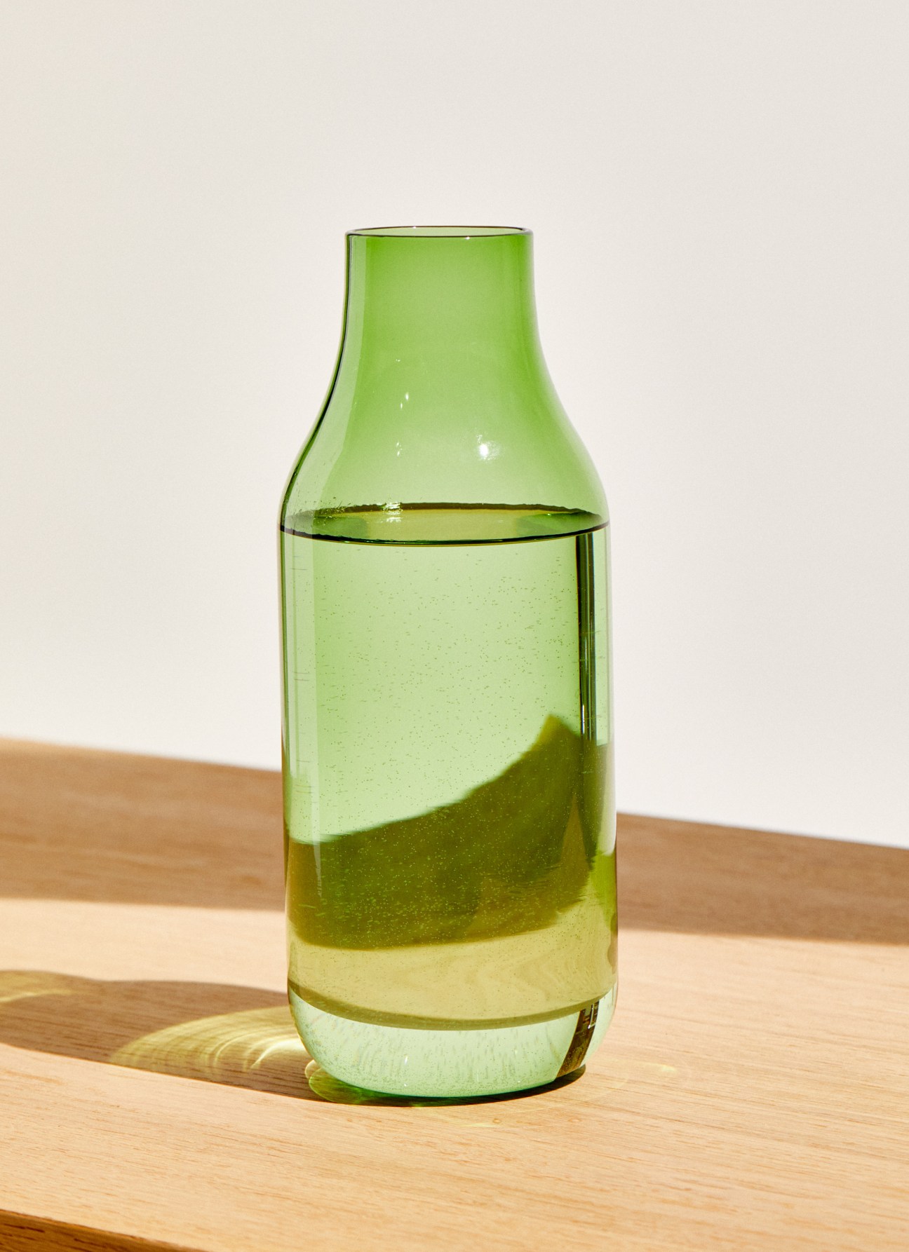 Green glass carafe with water on wooden surface against white background