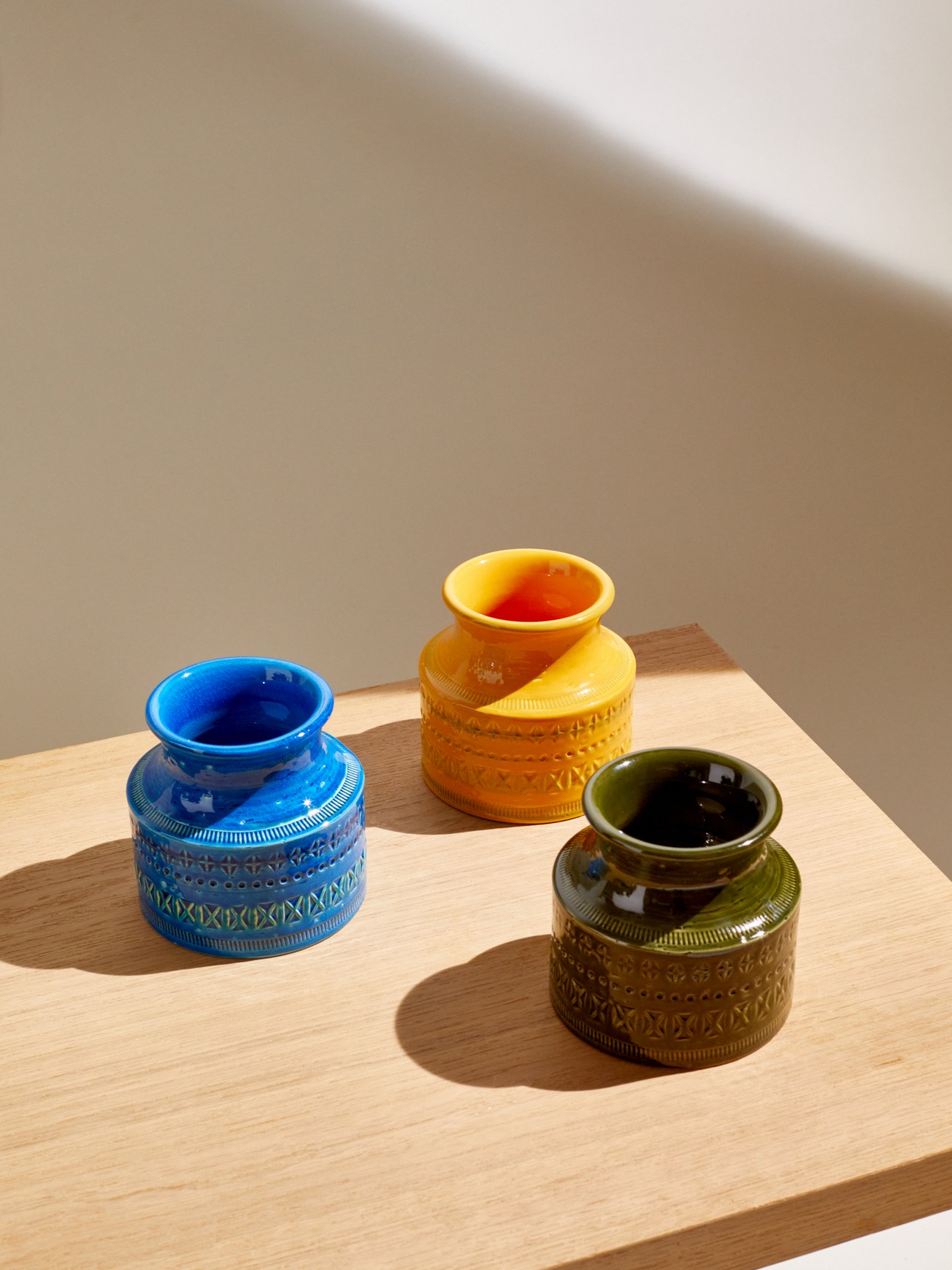 Three ceramic vases with decorative geometric patterns in blue, orange, and olive green colors on wooden surface