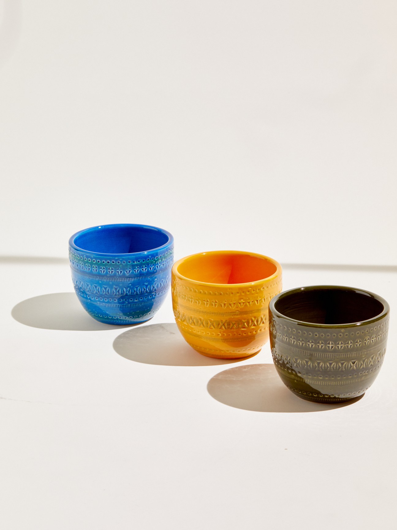 Three ceramic bowls with textured patterns in blue, yellow, and olive colors arranged on white surface
