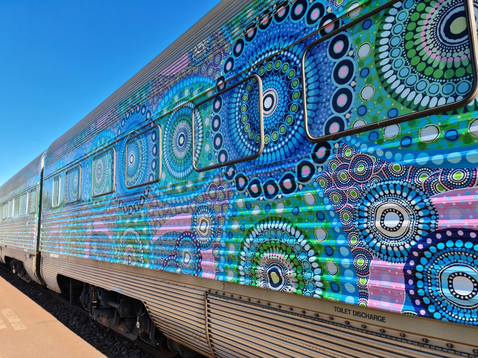 Colorfully painted train car with vibrant circular patterns and geometric designs in blues, greens, and other bright colors