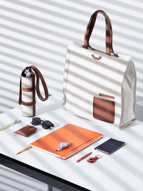 Water bottle holder by Métier, bag by Ermenegildo Zegna, sunglasses by Tod's, and accessories including notebook, pen, watch and key fob arranged on white surface.