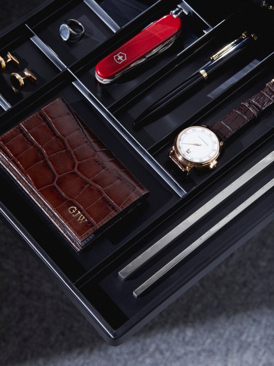 Luxury accessories including cufflinks, signet ring, Swiss Army knife, pen, watch, card case and rulers arranged in a display drawer.