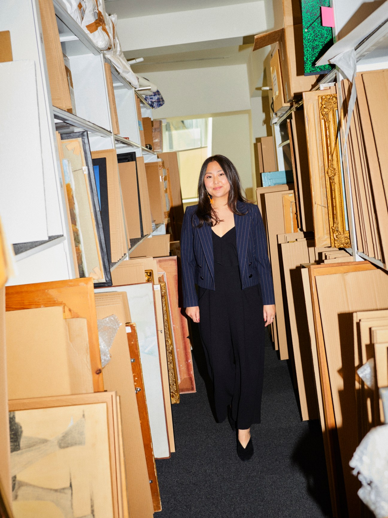 Cassi Young seated in auction house saleroom surrounded by framed artworks on shelves