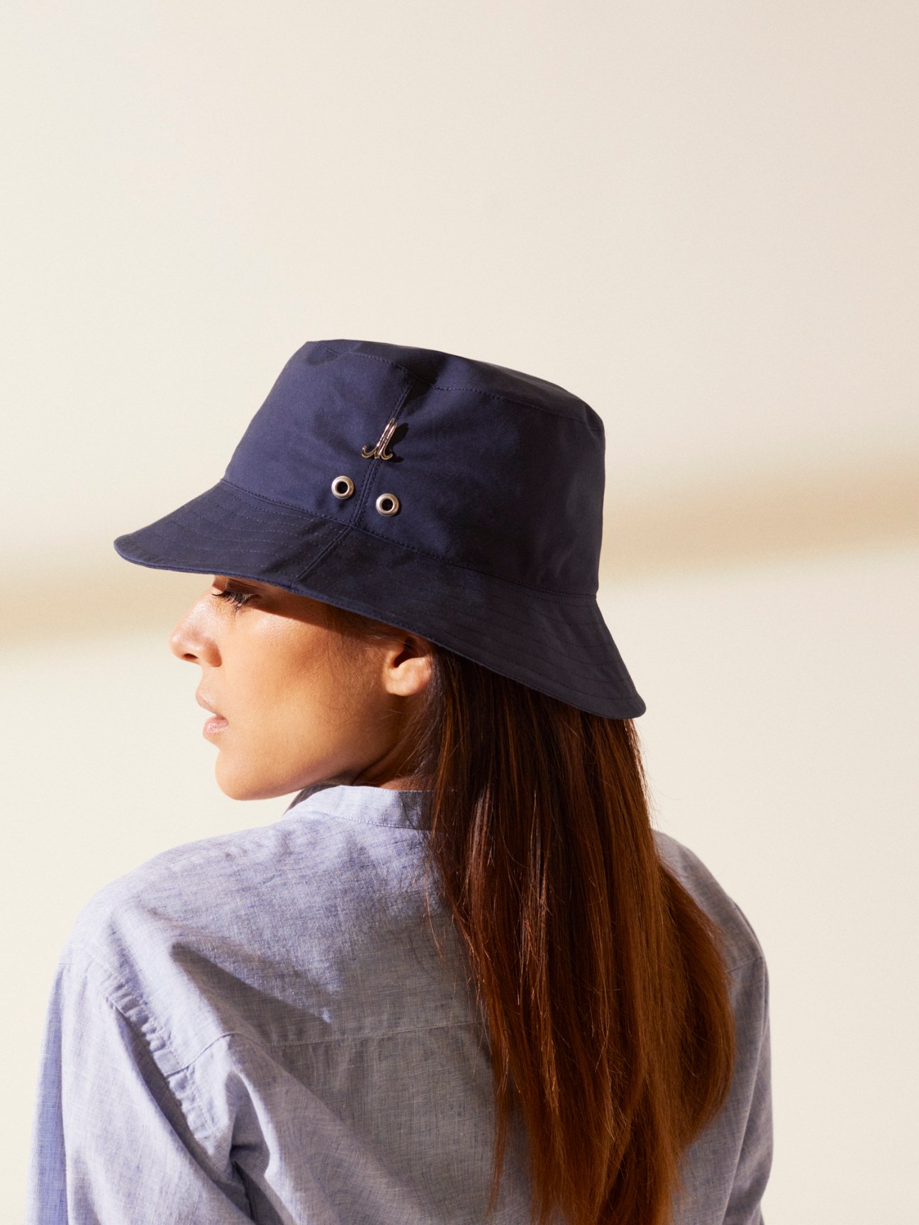 Woman in profile wearing navy Mühlbauer x Monocle tennis hat with adjustable strap and metal grommets