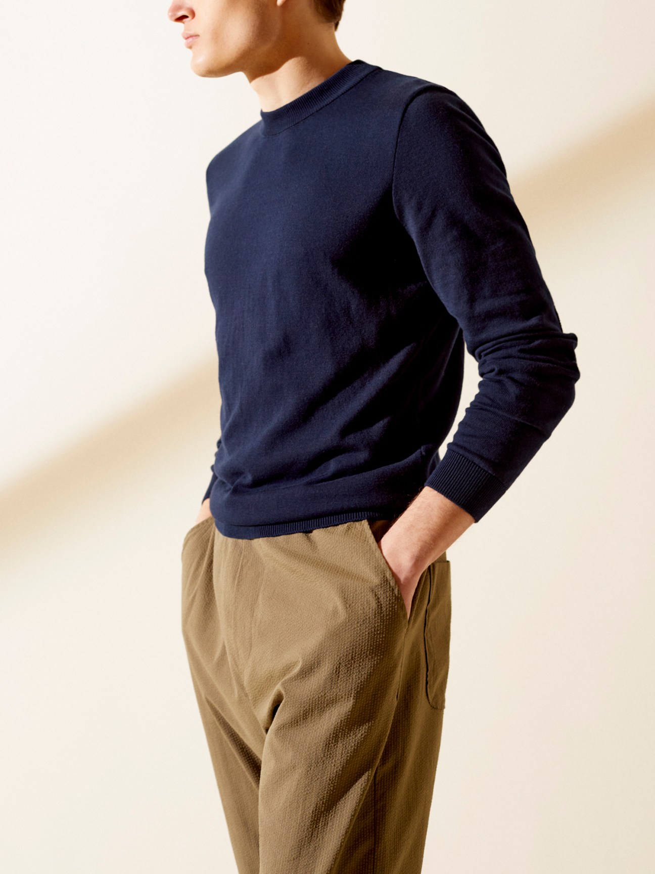 Man wearing navy cotton crewneck pullover and beige trousers in three-quarter view