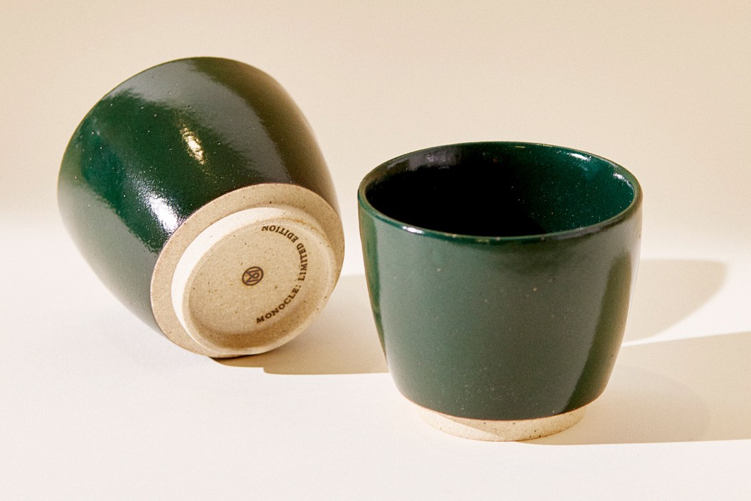 Two forest-green Monocle Yunomi cups, one tilted to show the bottom with maker's mark, one upright