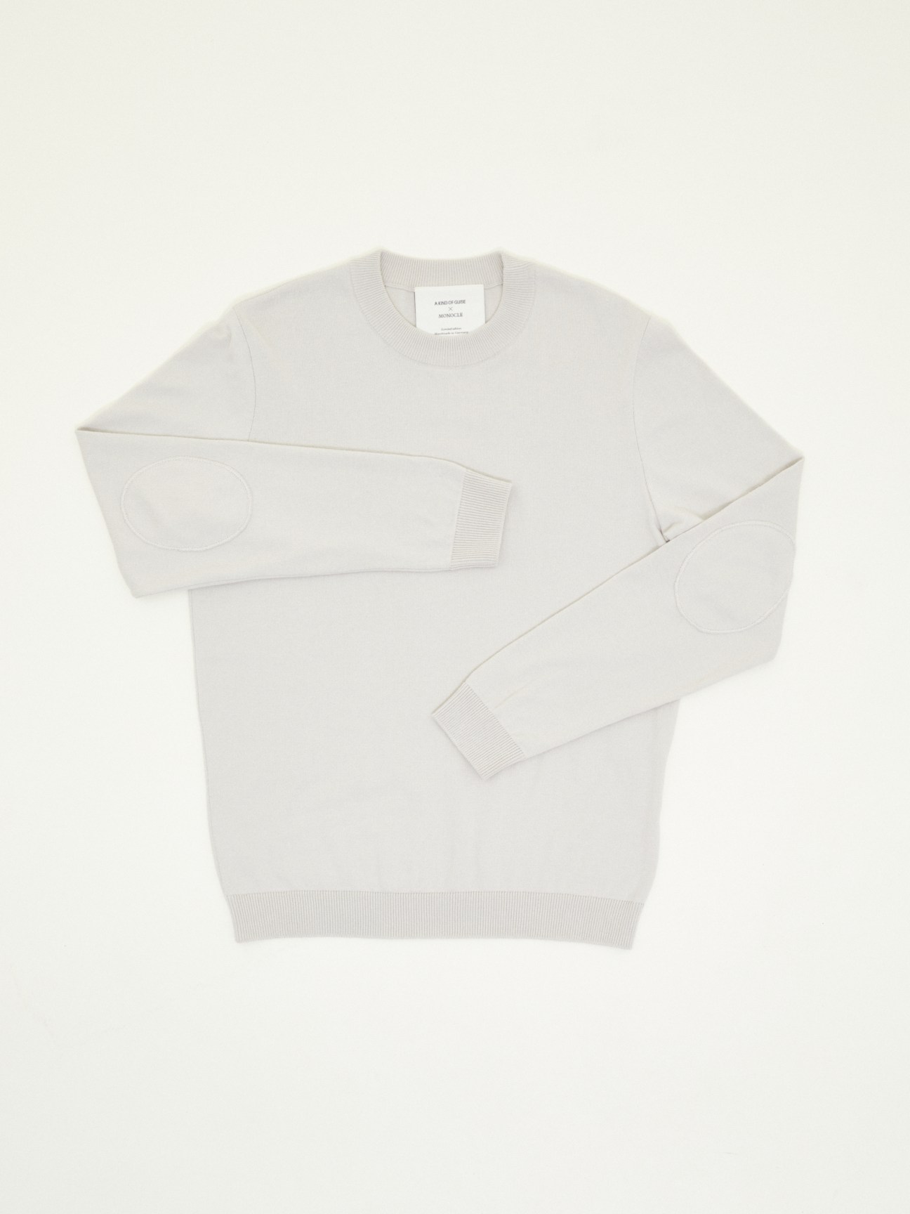 A Kind of Guise x Monocle cotton pullover in stone color displayed flat against a neutral background.