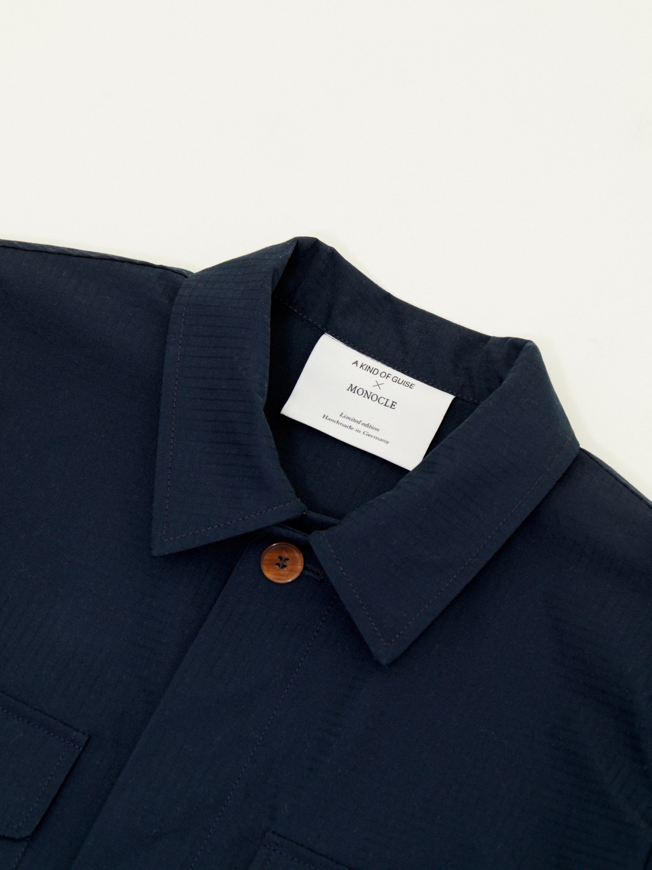 Close-up detail of navy safari jacket collar and button showing A Kind of Guise x Monocle collaboration label