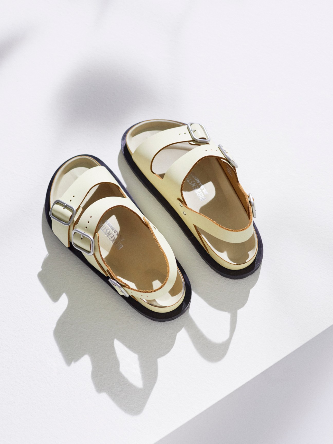 Cream colored leather sandals with double buckle straps and thick soles against white background