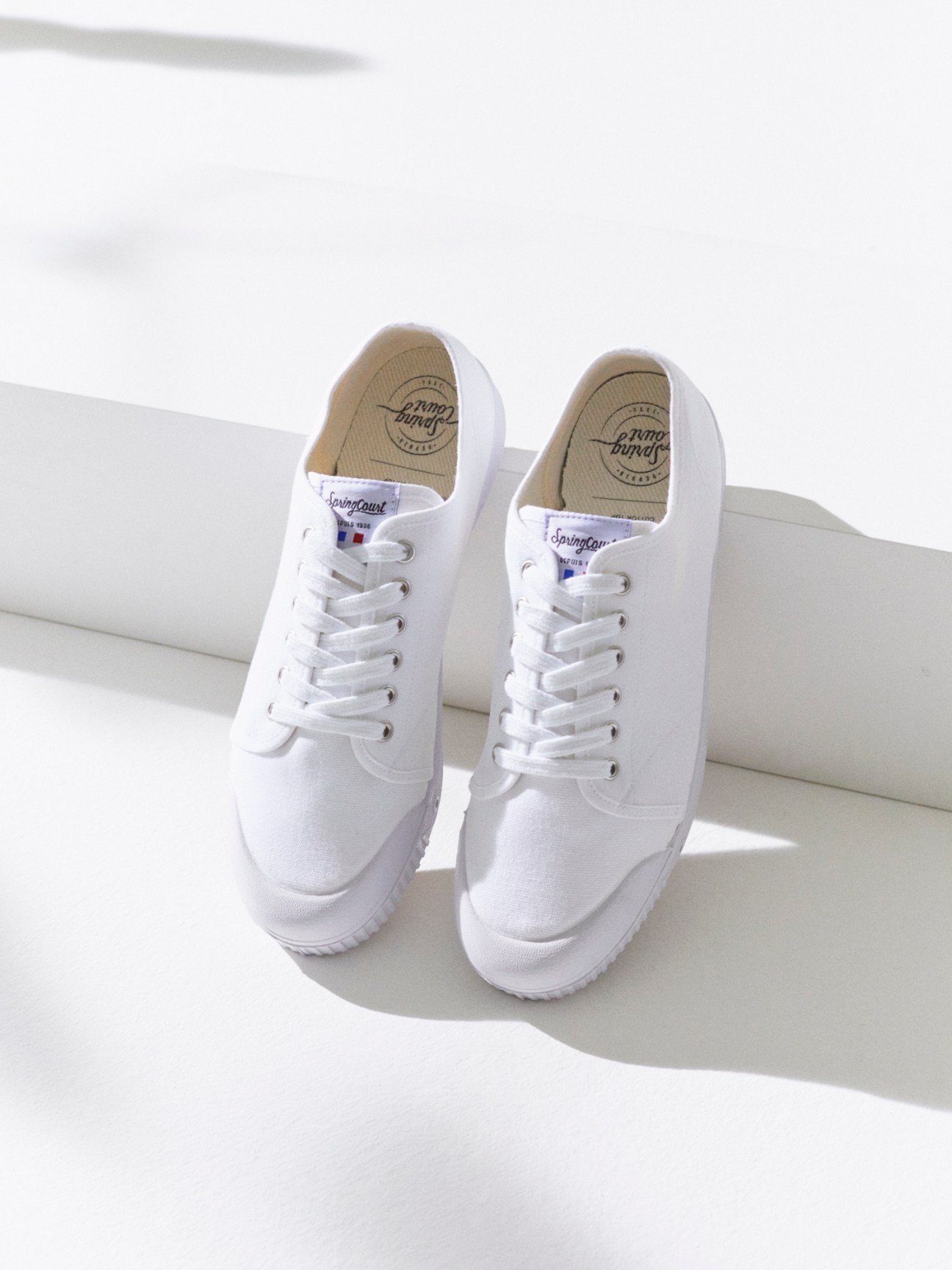 White canvas sneakers with laces positioned on white steps in bright sunlight