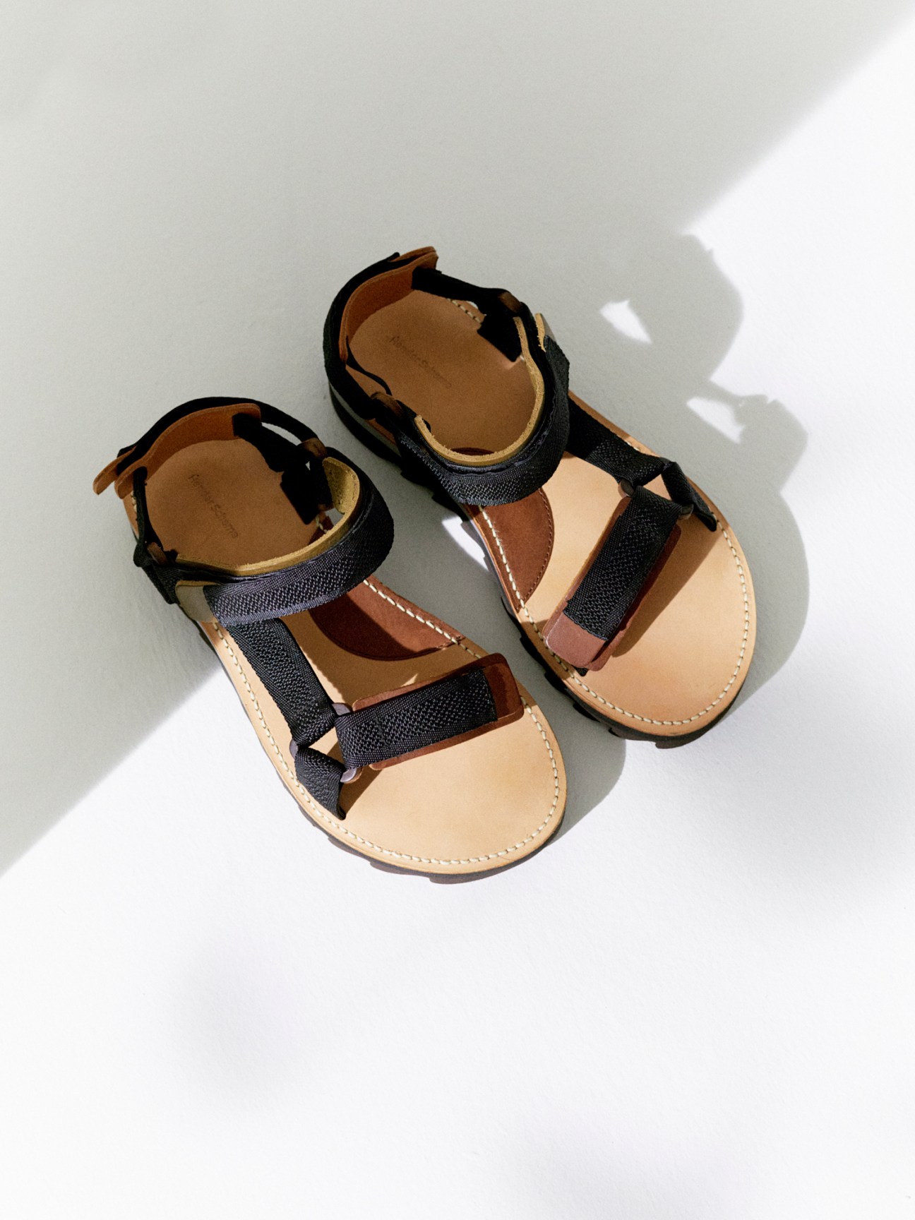 Natural leather sandals with woven black straps and minimalist design against white background
