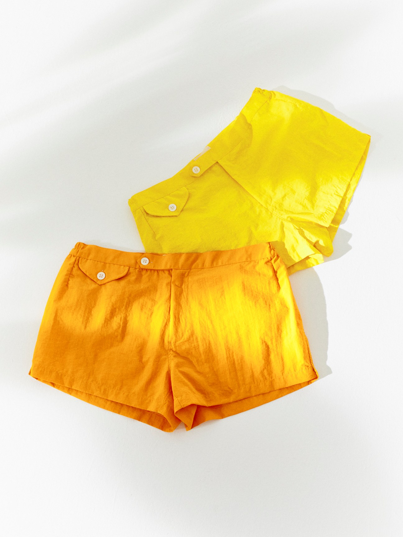 Yellow and orange swim shorts with button details and elastic waistbands laid flat against white background