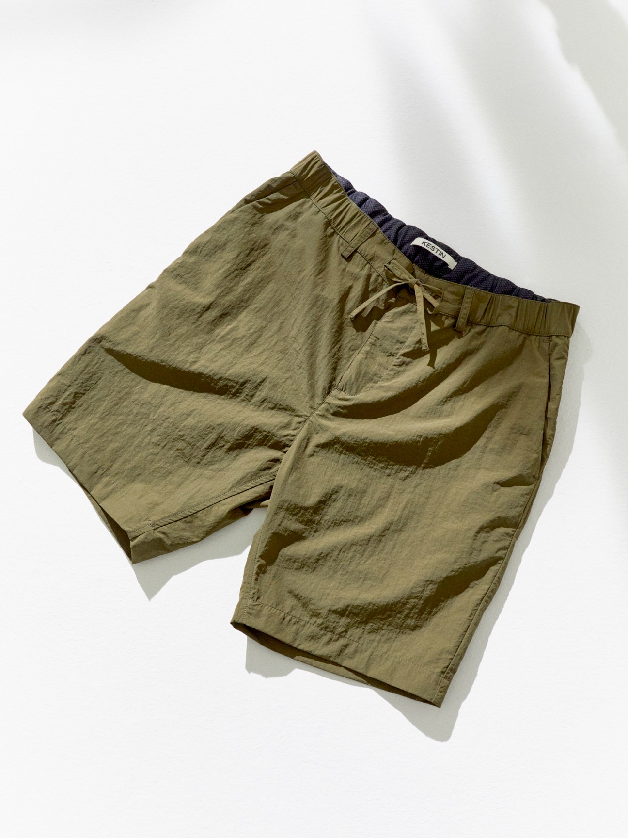 Olive green tailored shorts with drawstring waist and navy waistband detail laid flat against white background