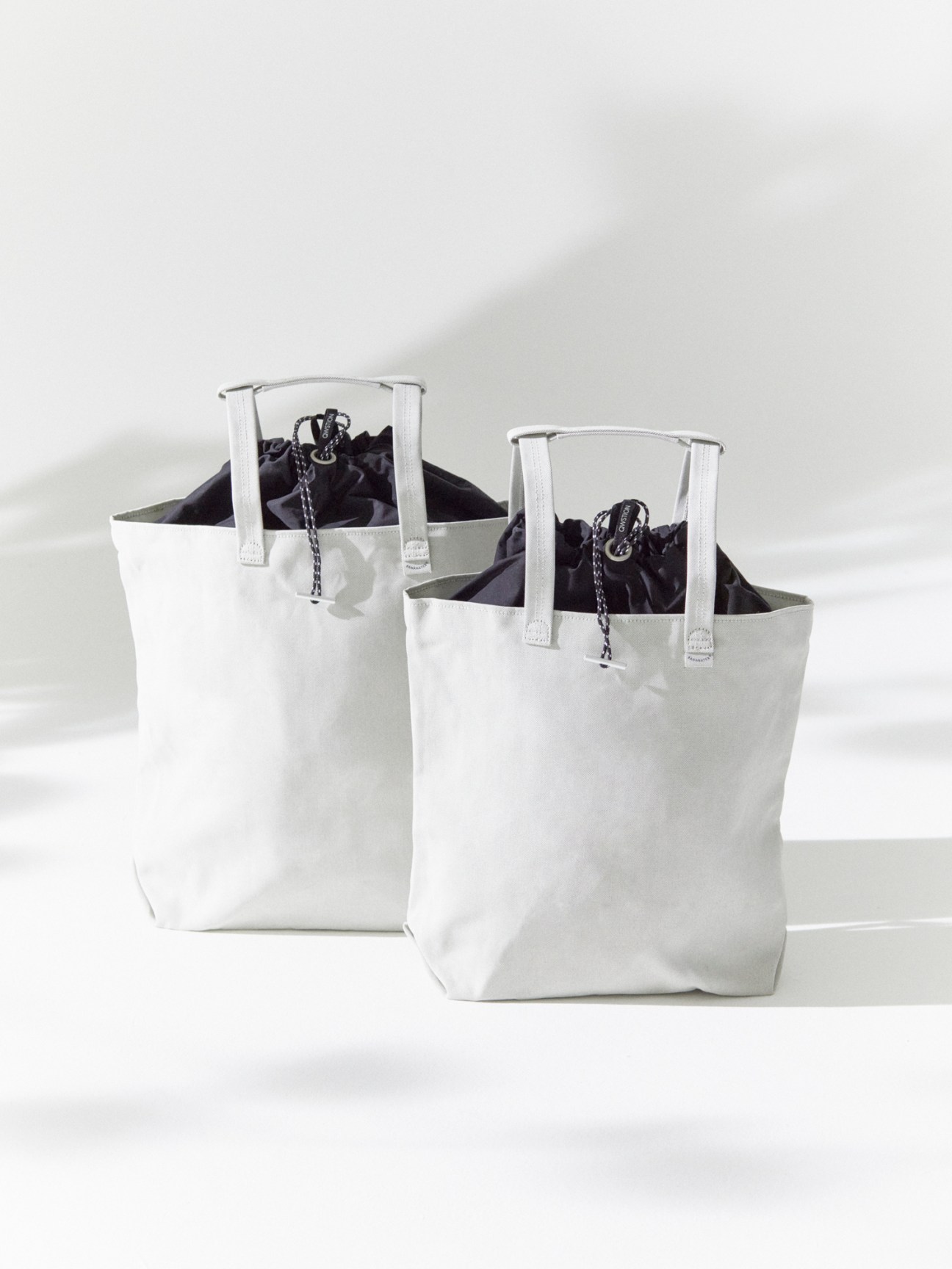 Two light gray canvas tote bags with white leather handles and black interior pouches