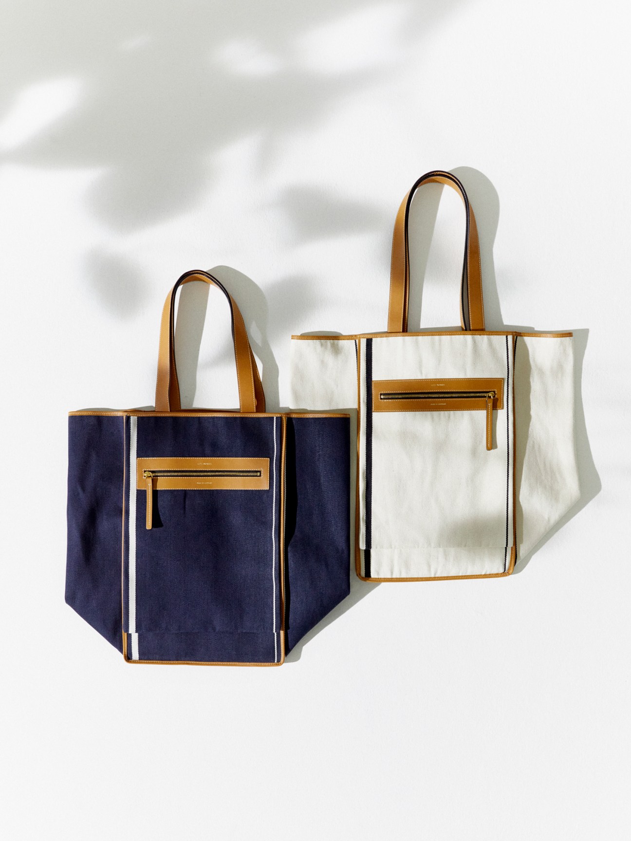 Two structured tote bags in navy and cream with leather trim and zippered front pockets