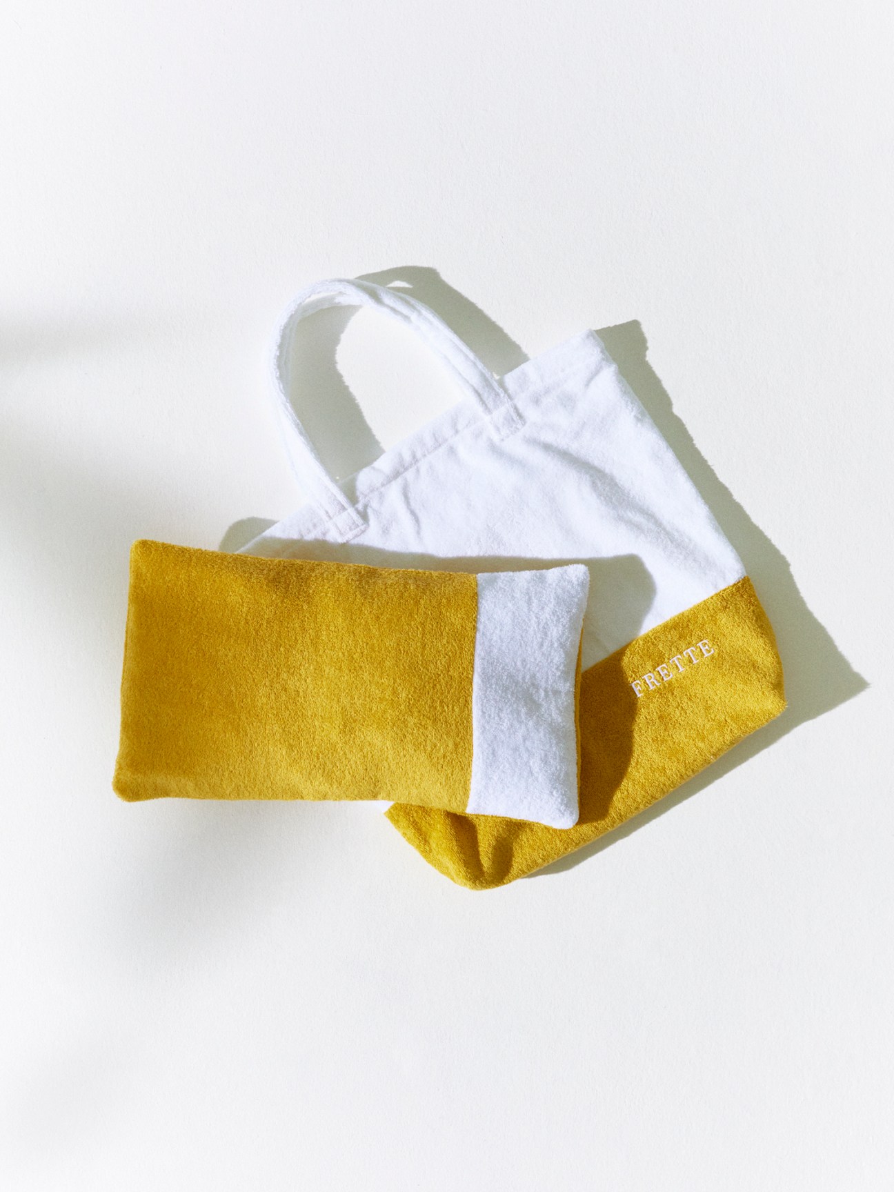 Yellow terry cloth beach bag and matching cushion with white trim by Frette against white background