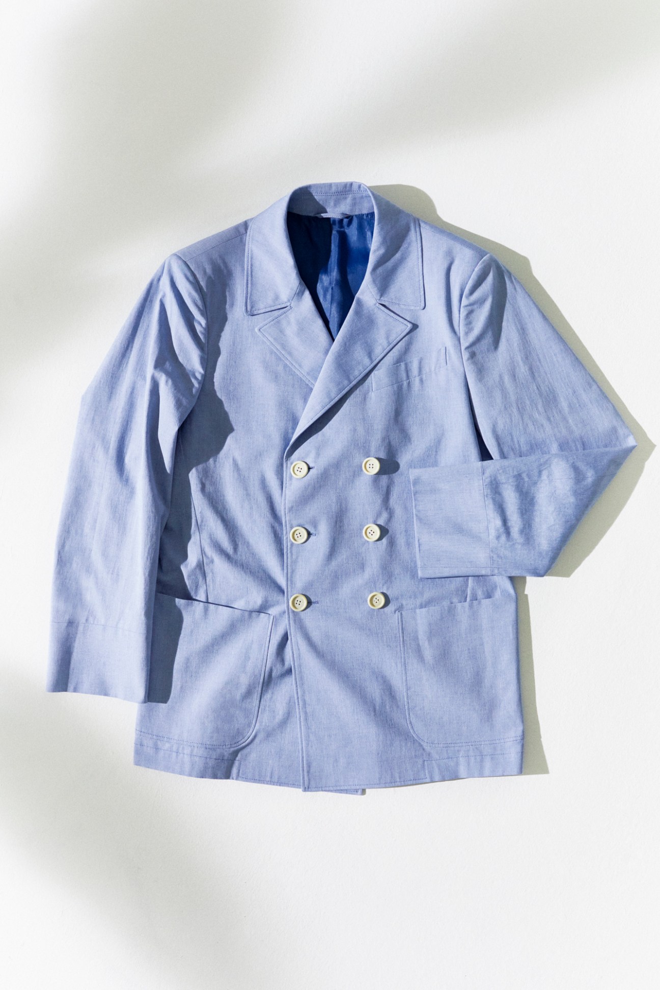 Light blue double-breasted jacket with white buttons laid flat against white background
