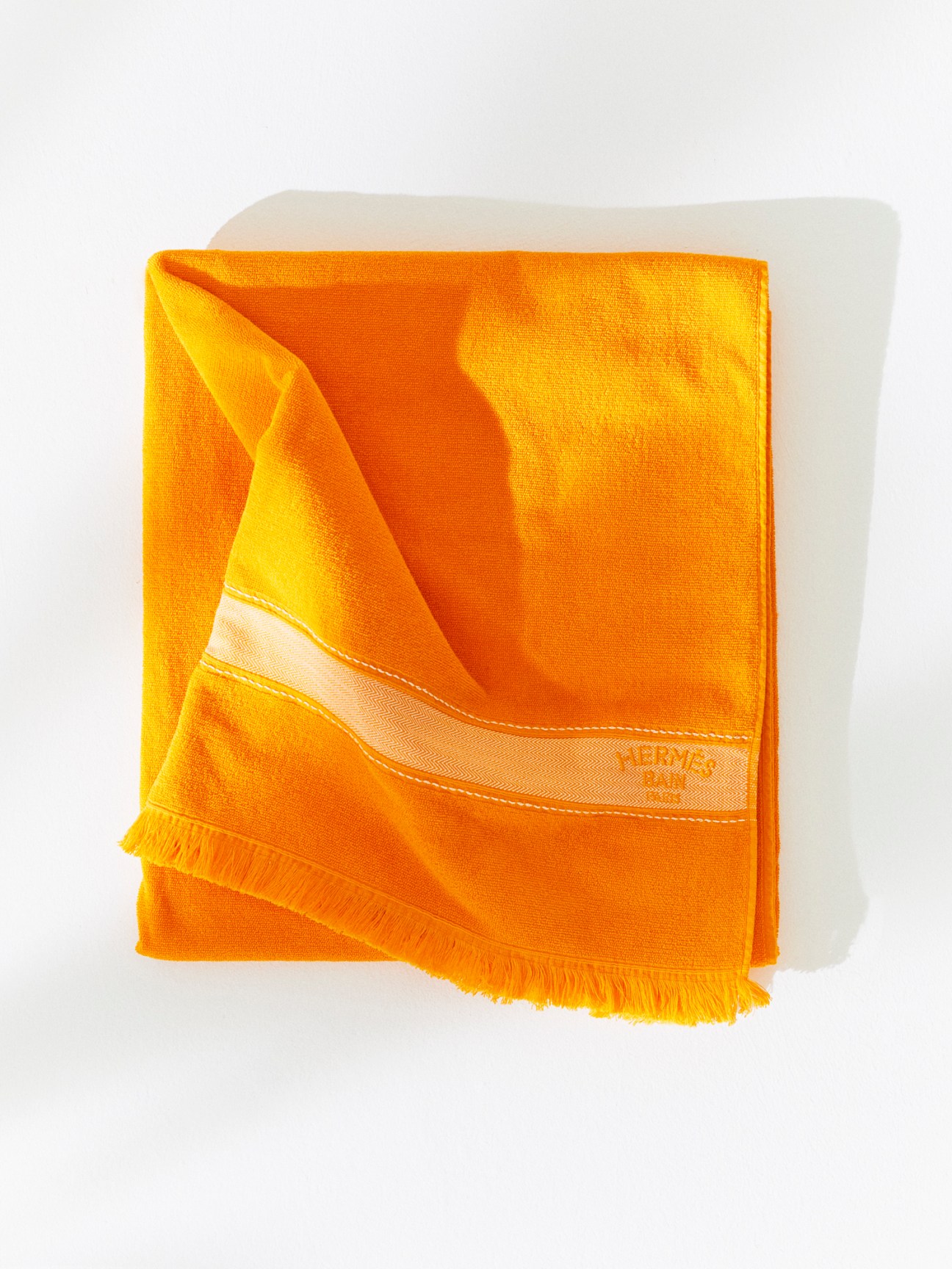 Bright orange Hermès beach towel with fringe edges folded against white background