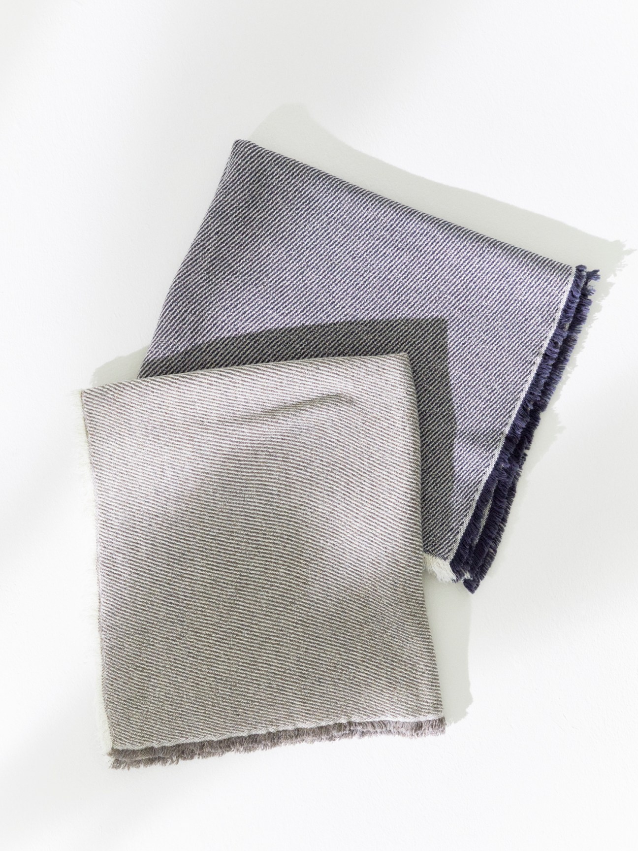 Two folded striped towels in gray and white with fringed edges by Kontex