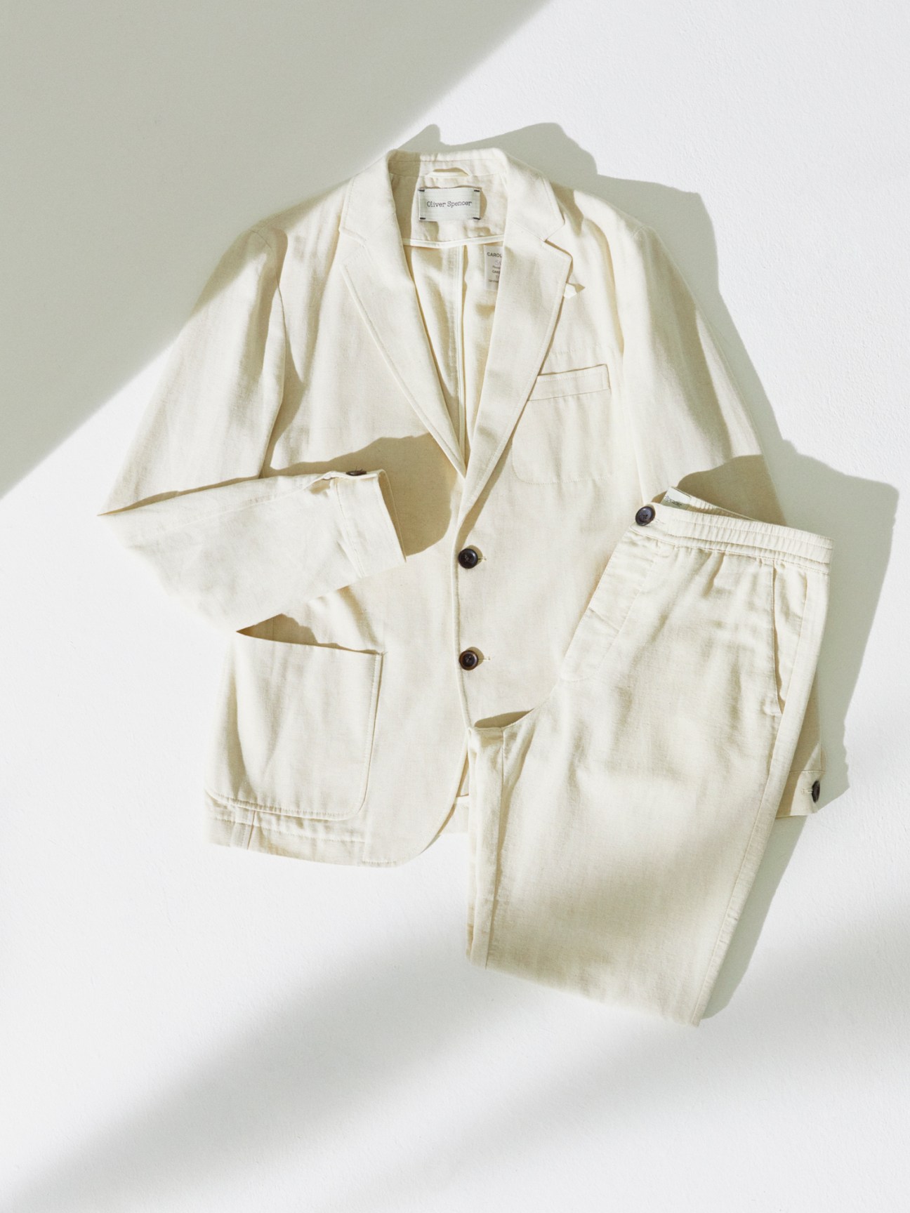 Light colored linen blazer and matching trousers laid flat against white background