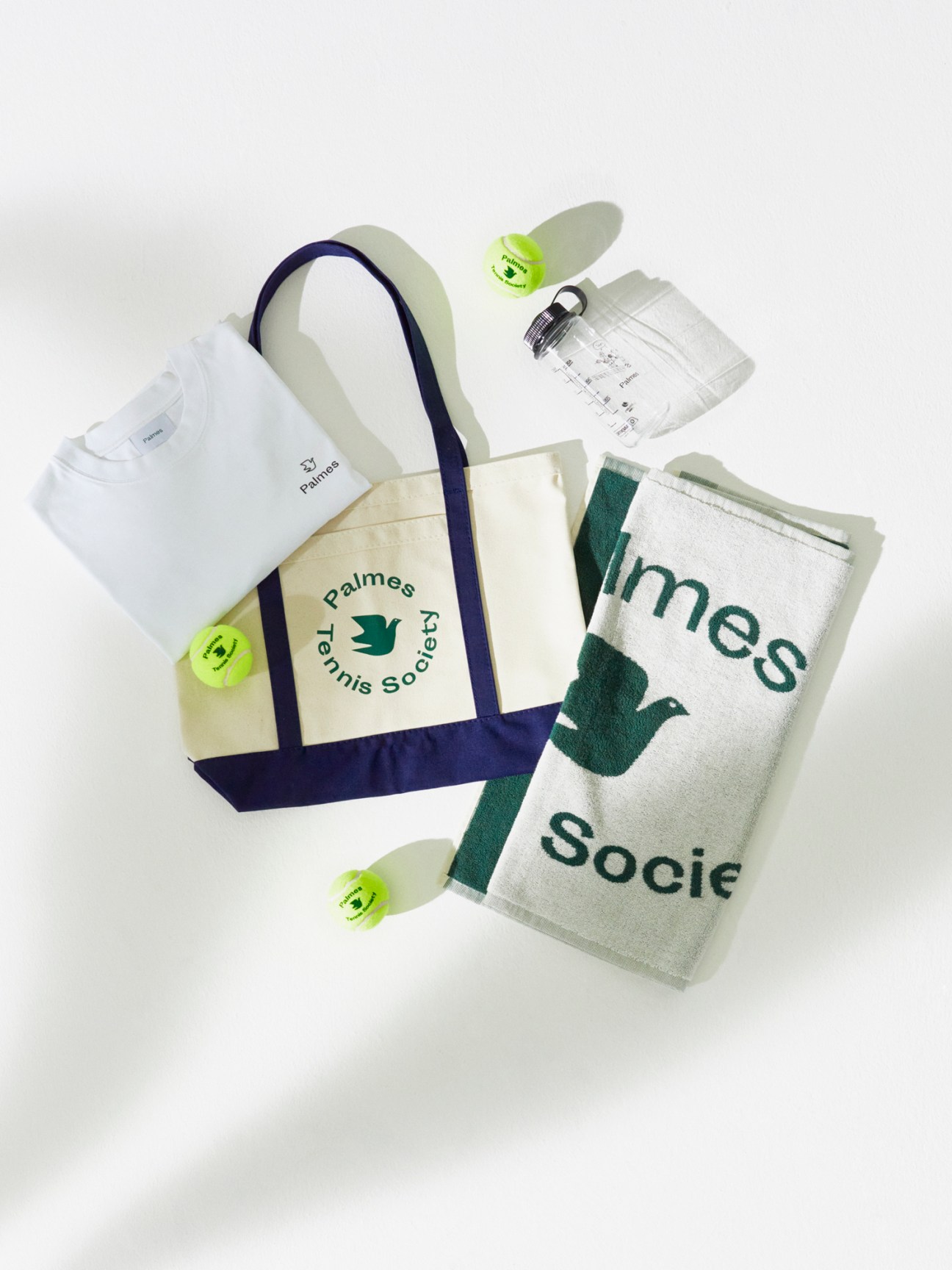 Tennis accessories including white t-shirt, canvas tote bag, towel, water bottle and bright tennis balls by Palmes