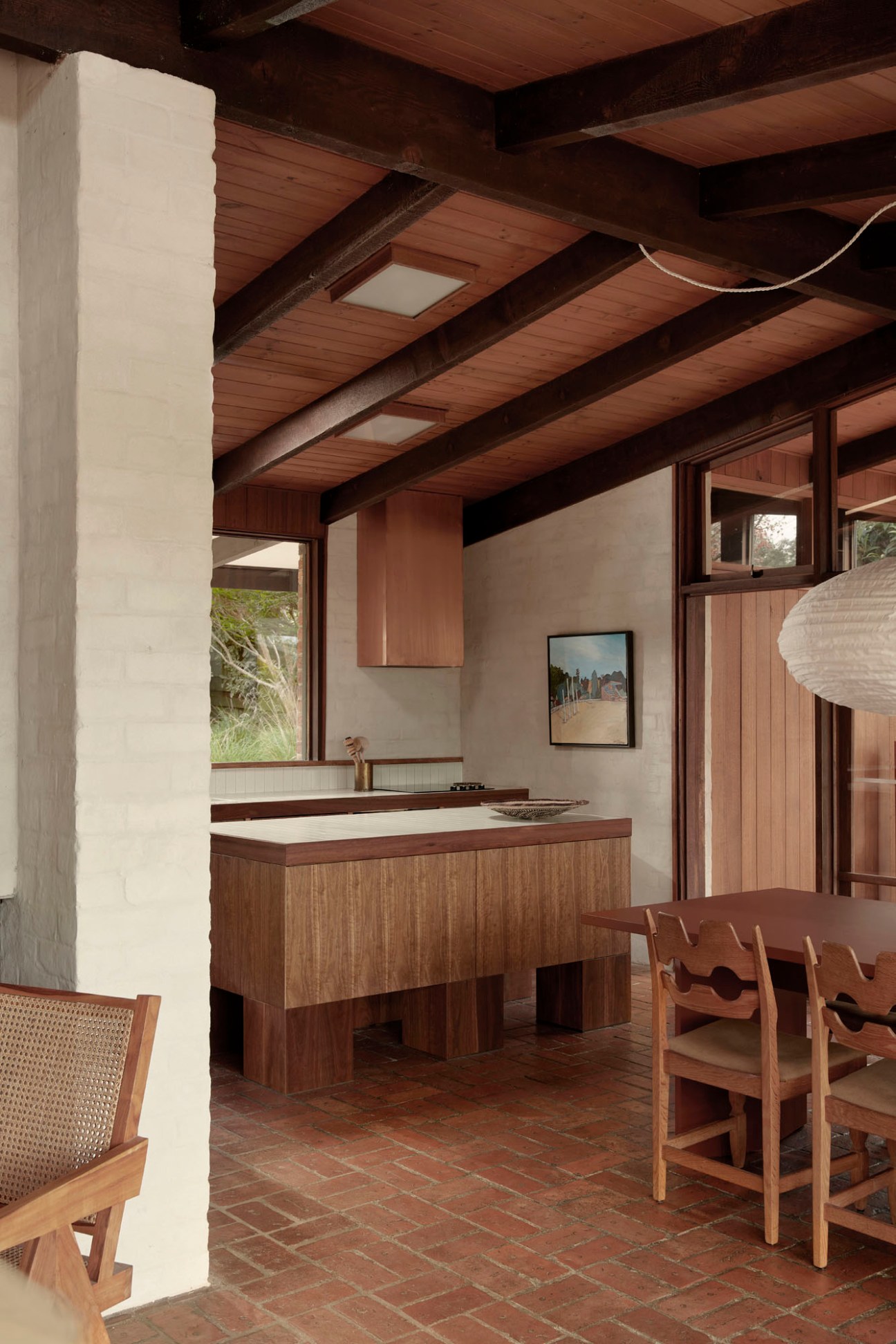 Modernist kitchen and dining area with timber cabinetry, brick floors, exposed wooden beams and skylights.