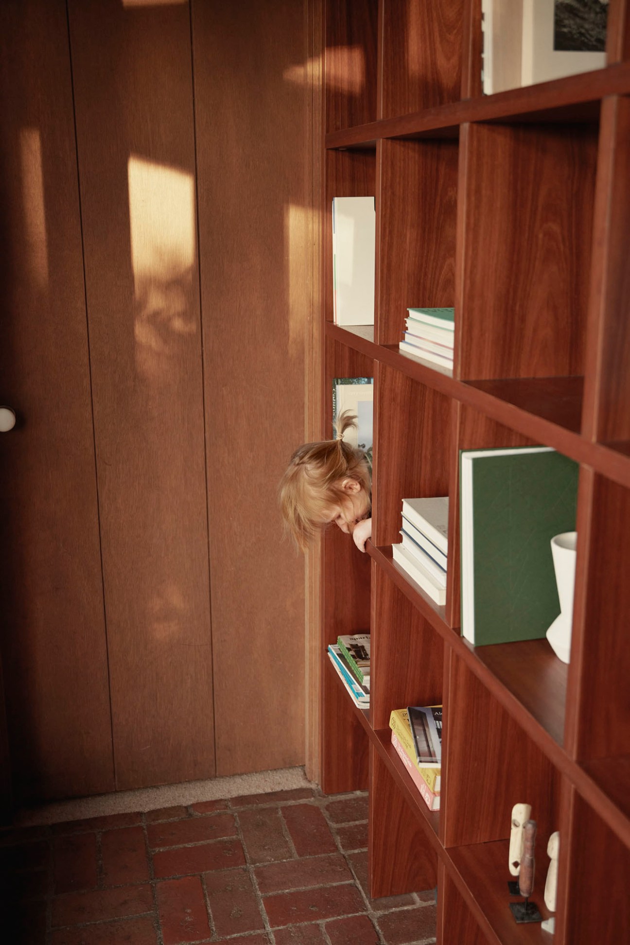 A young child peeks through wooden shelving unit in a modernist home interior.