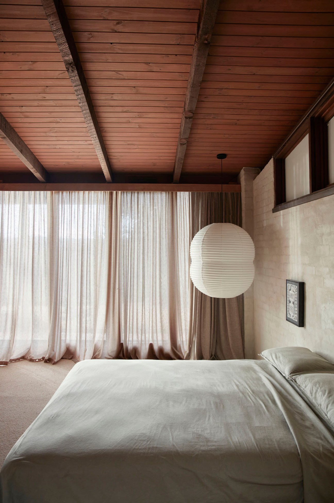 Master bedroom with wooden beamed ceiling, white bed, flowing curtains, and pendant light fixture.
