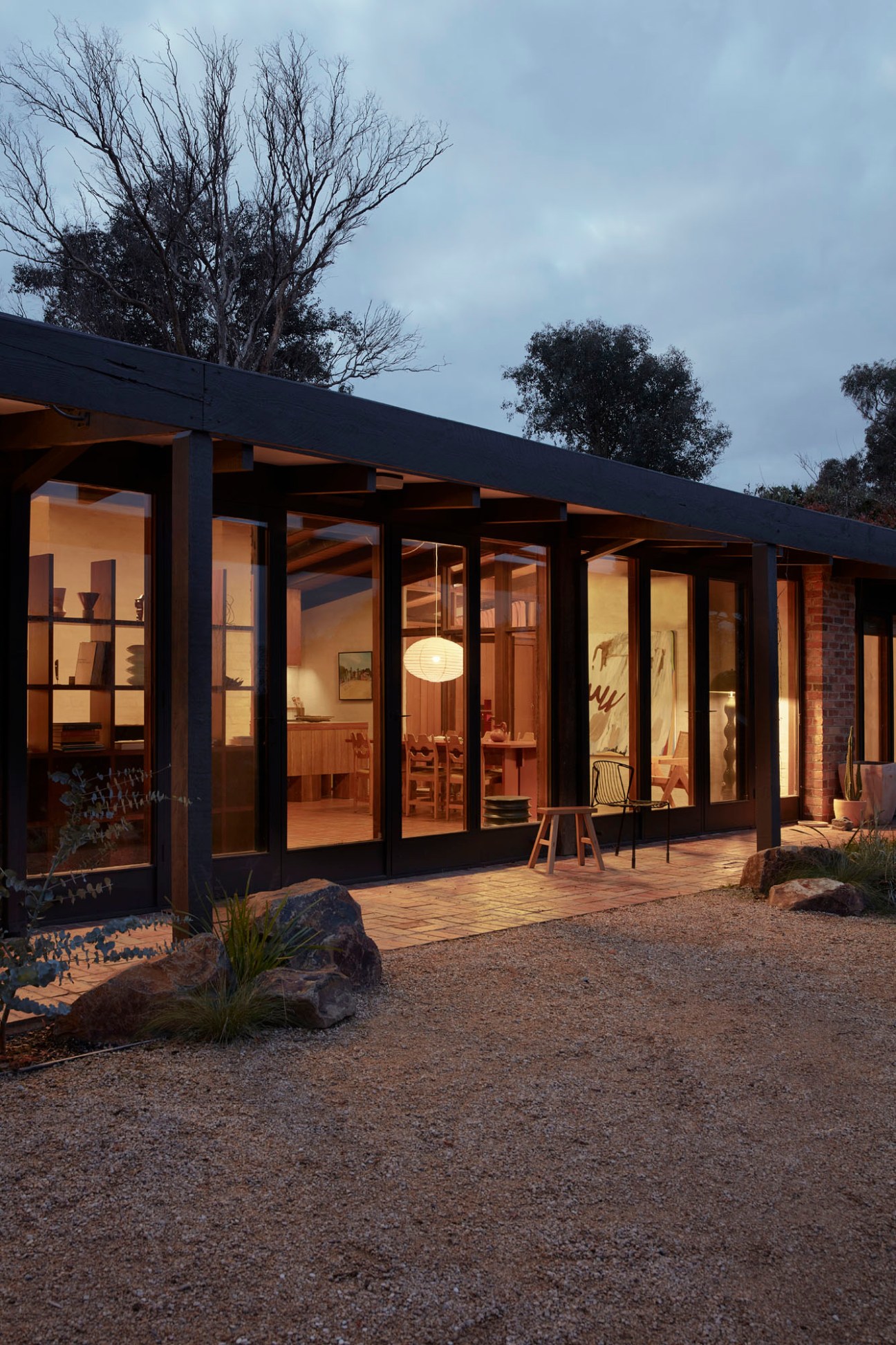 Modern renovation of 1969 modernist house with black frame and glass doors opening onto courtyard at dusk.
