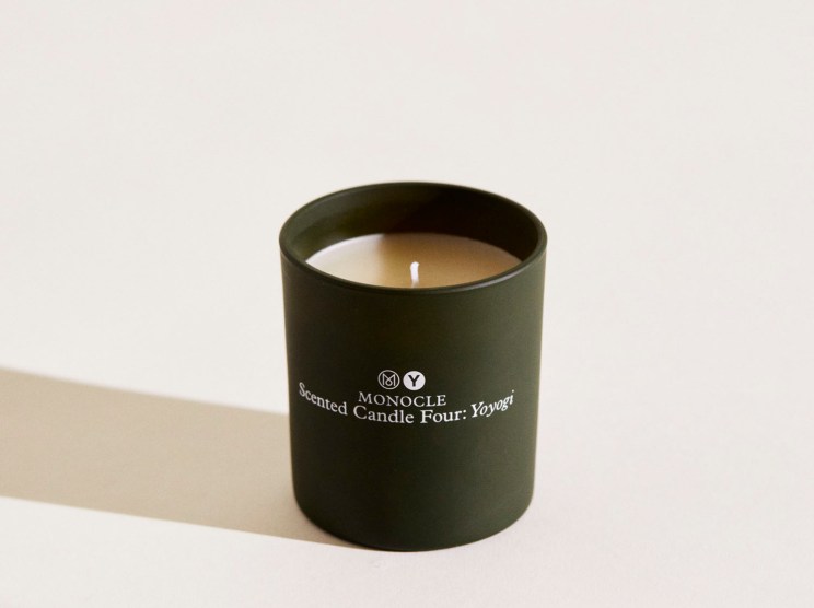 Dark green cylindrical candle in container with Monocle branding and white wick