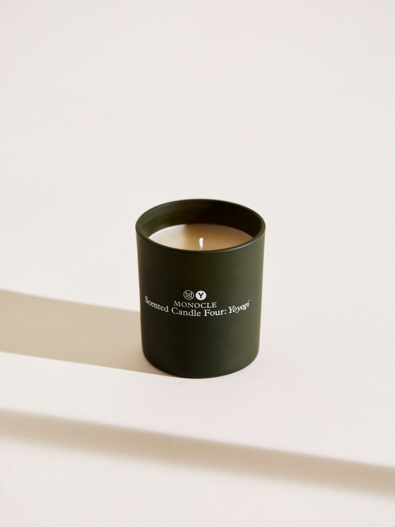 Dark green cylindrical candle in container with Monocle branding and white wick